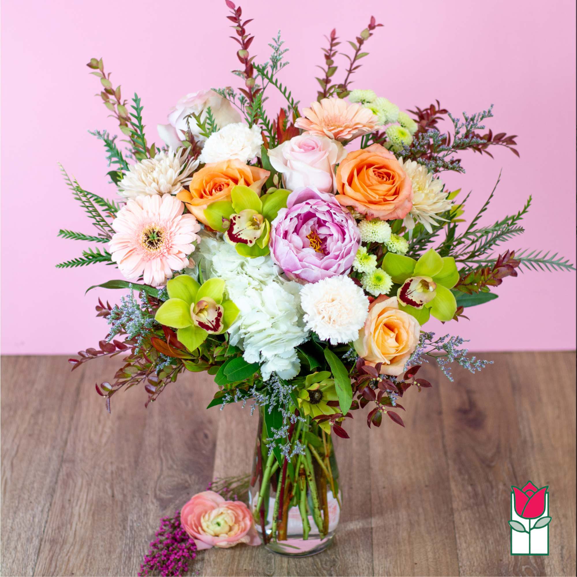Mixed bouquet of roses, peonies, and orchids in a glass vase