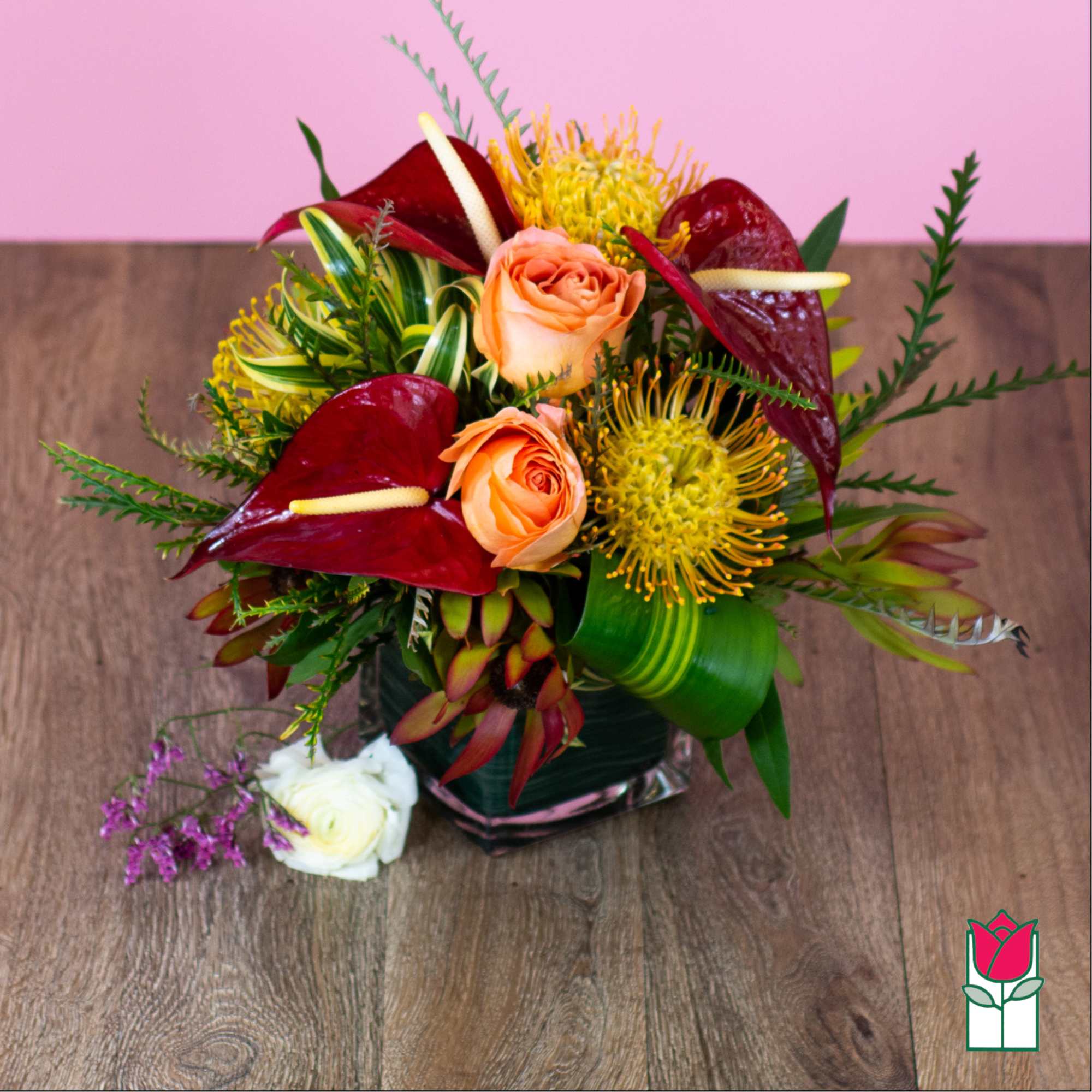 Tropical bouquet with peach roses, burgundy anthuriums, and yellow pincushion blooms in a glass vase