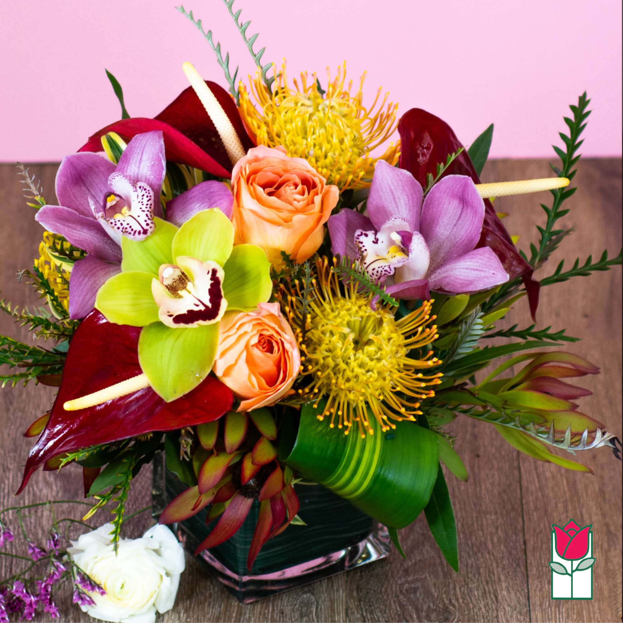 Tropical bouquet with orchids, roses, and yellow pincushion blooms in a glass vase, photo 3 of 5