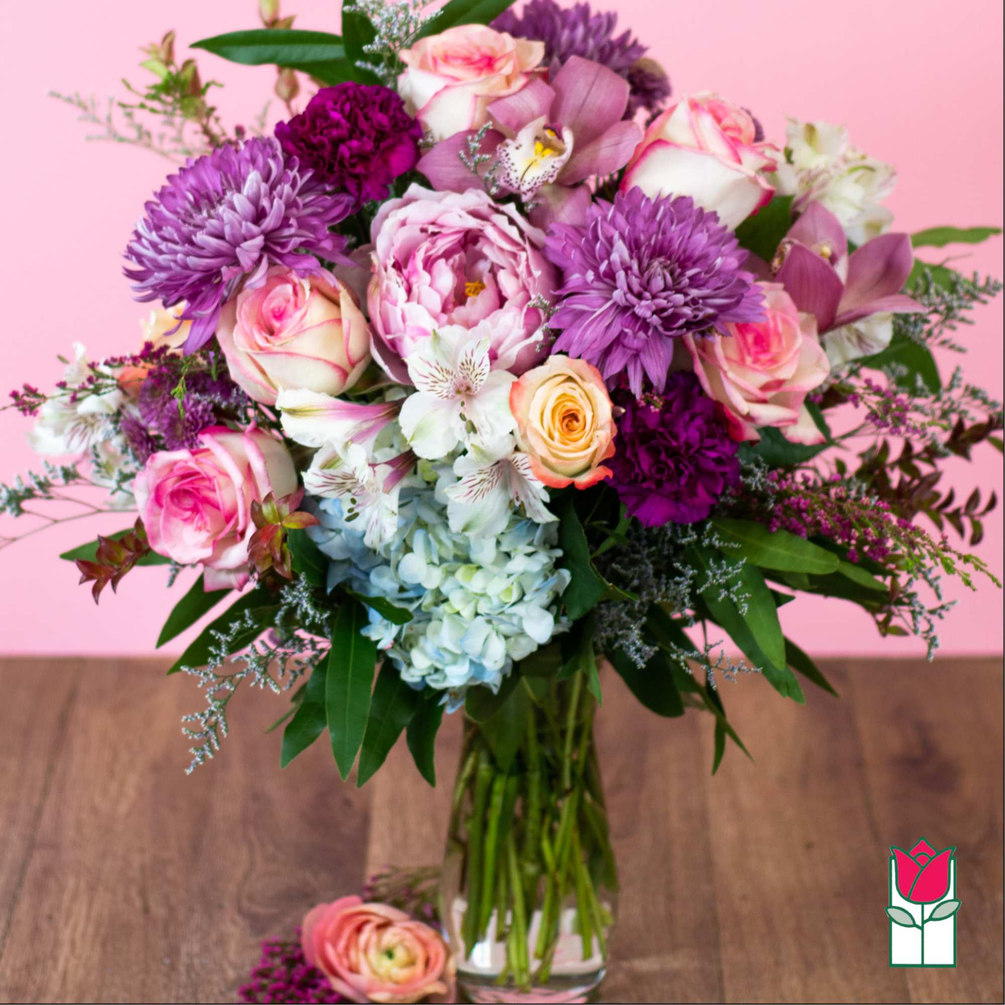 Mixed bouquet of pink roses, purple mums, orchids, and hydrangea in a clear glass vase