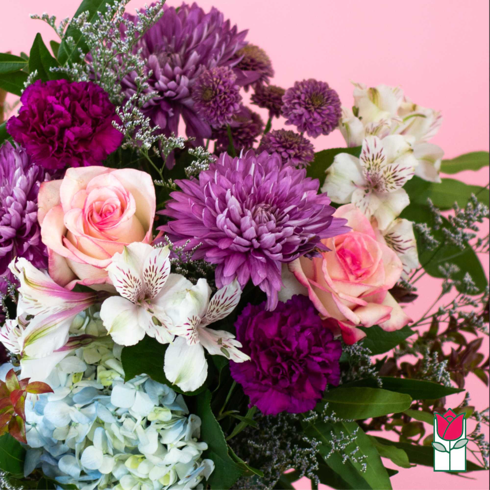 Bouquet of purple mums, pink roses, white alstroemeria, and blue hydrangea on a pink background