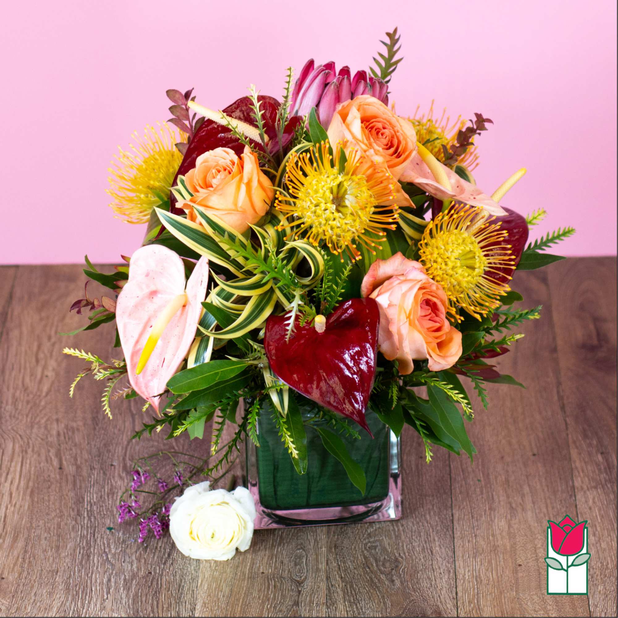 Mixed bouquet with peach roses and tropical blooms in a square glass vase