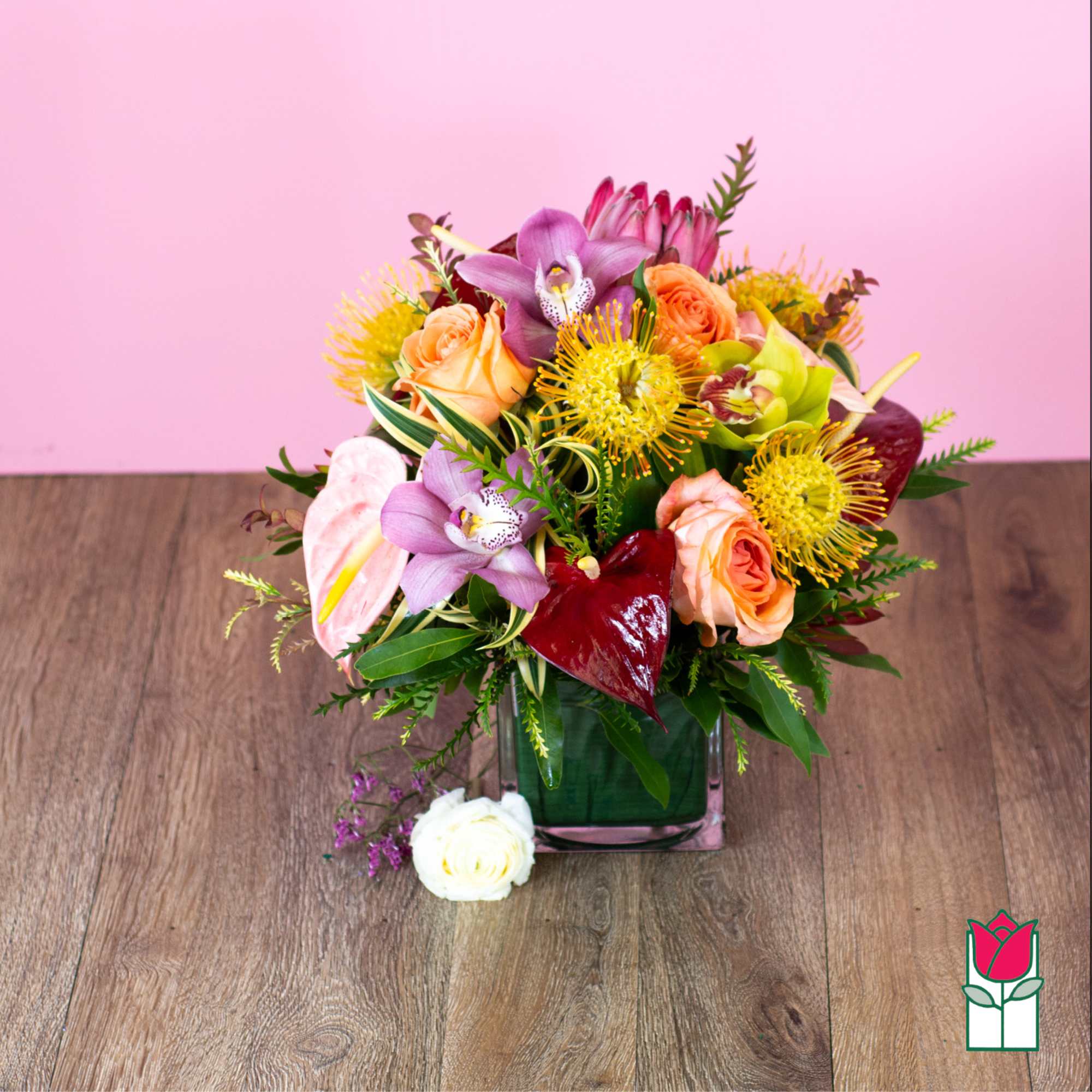 Mixed bouquet in a square glass vase with orchids, roses, and anthuriums