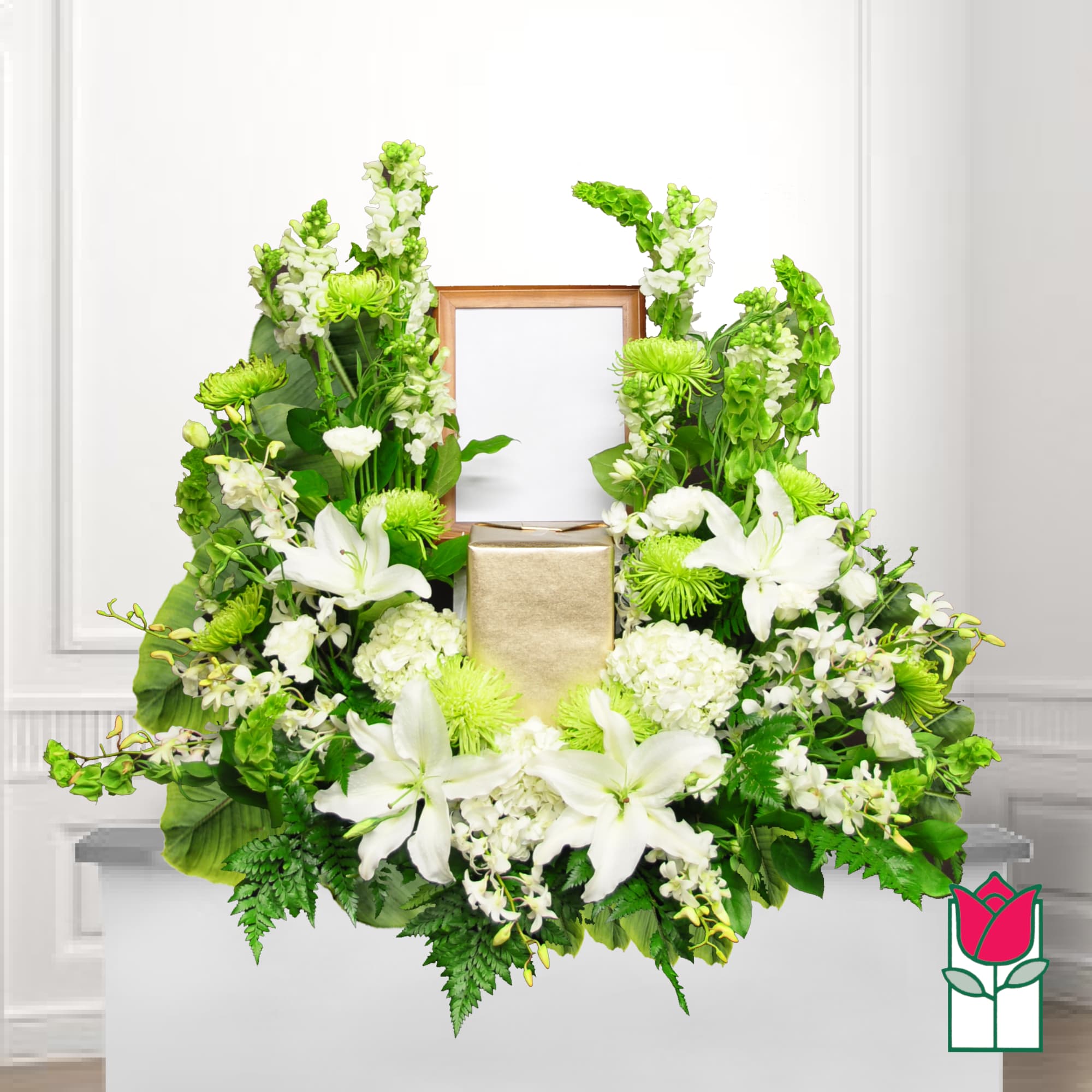 White lilies and green flowers arranged around a gold urn and frame