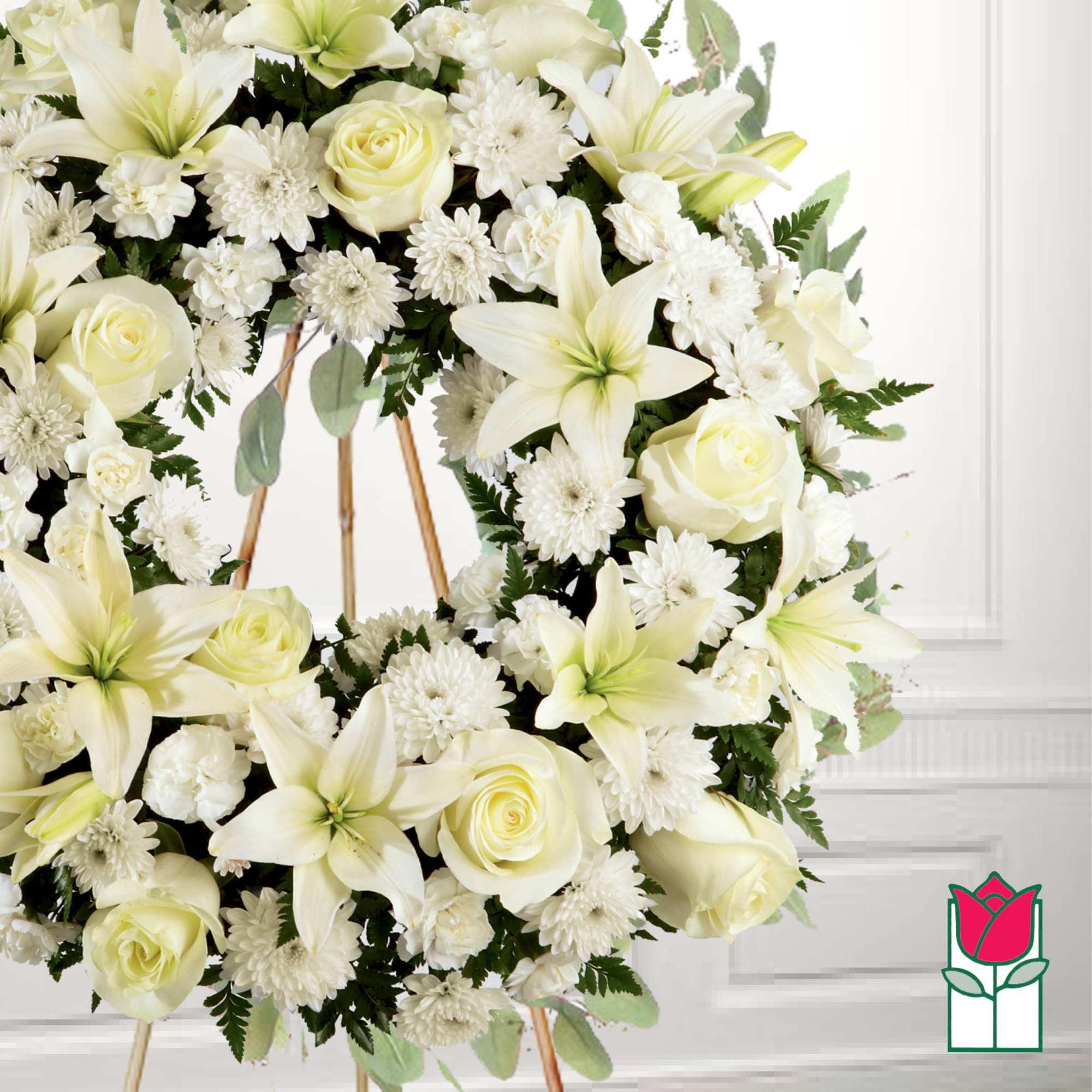 White floral wreath with lilies, roses, and daisies on a stand