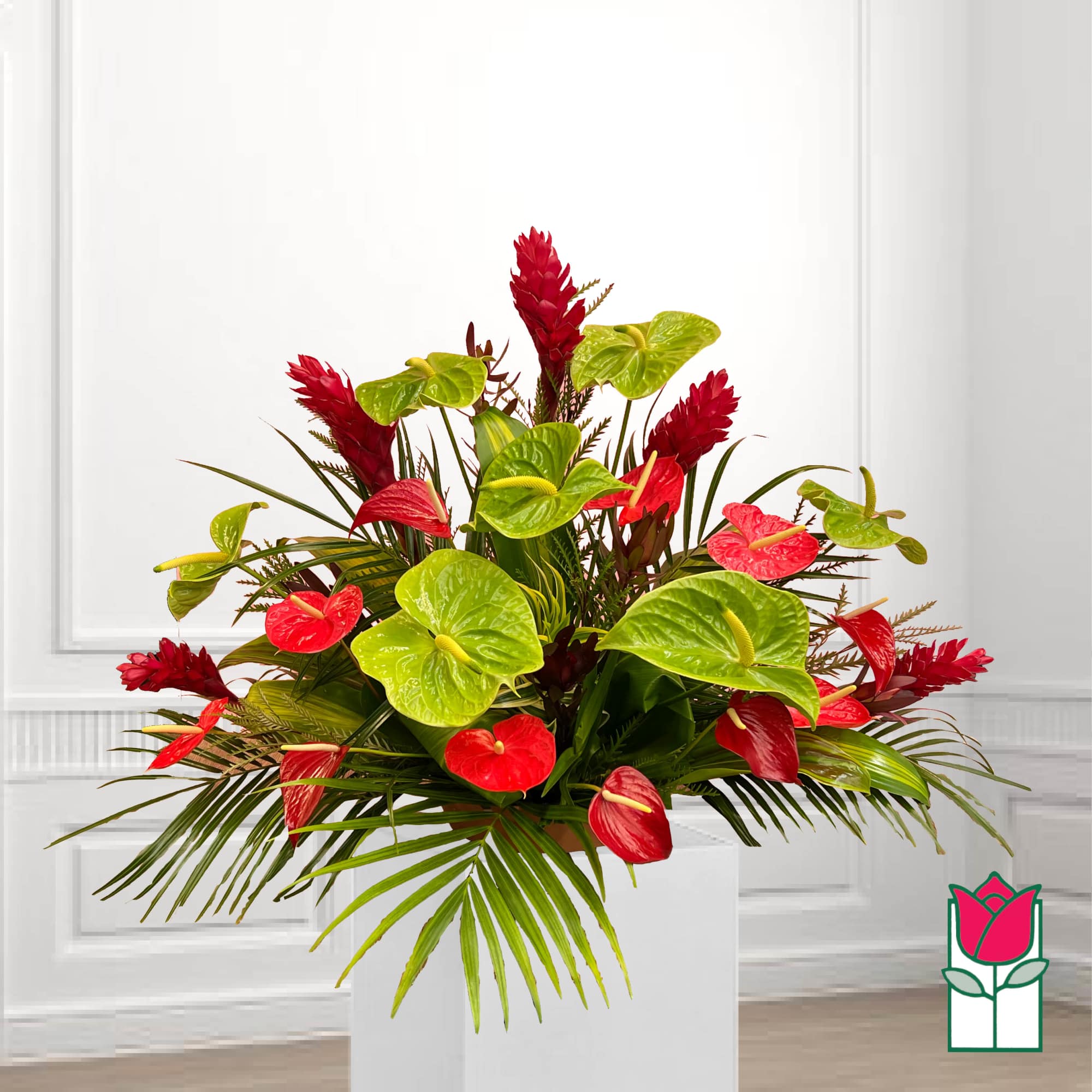 Red and green tropical floral arrangement in a white container