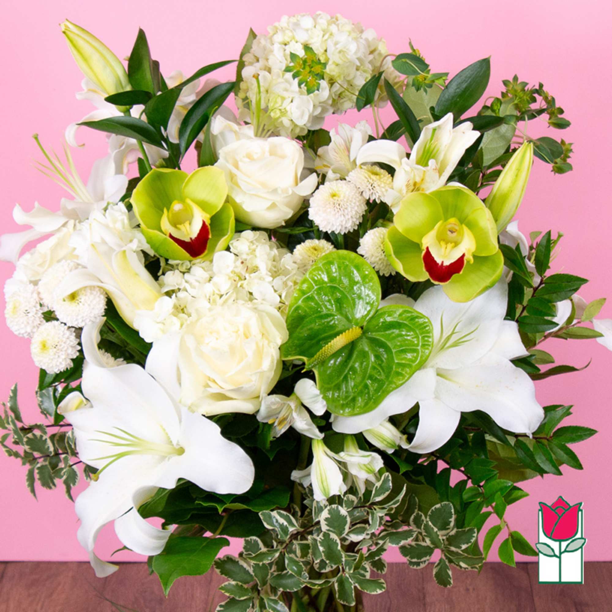 White lilies, roses, and green orchids in a lush bouquet on a pink background