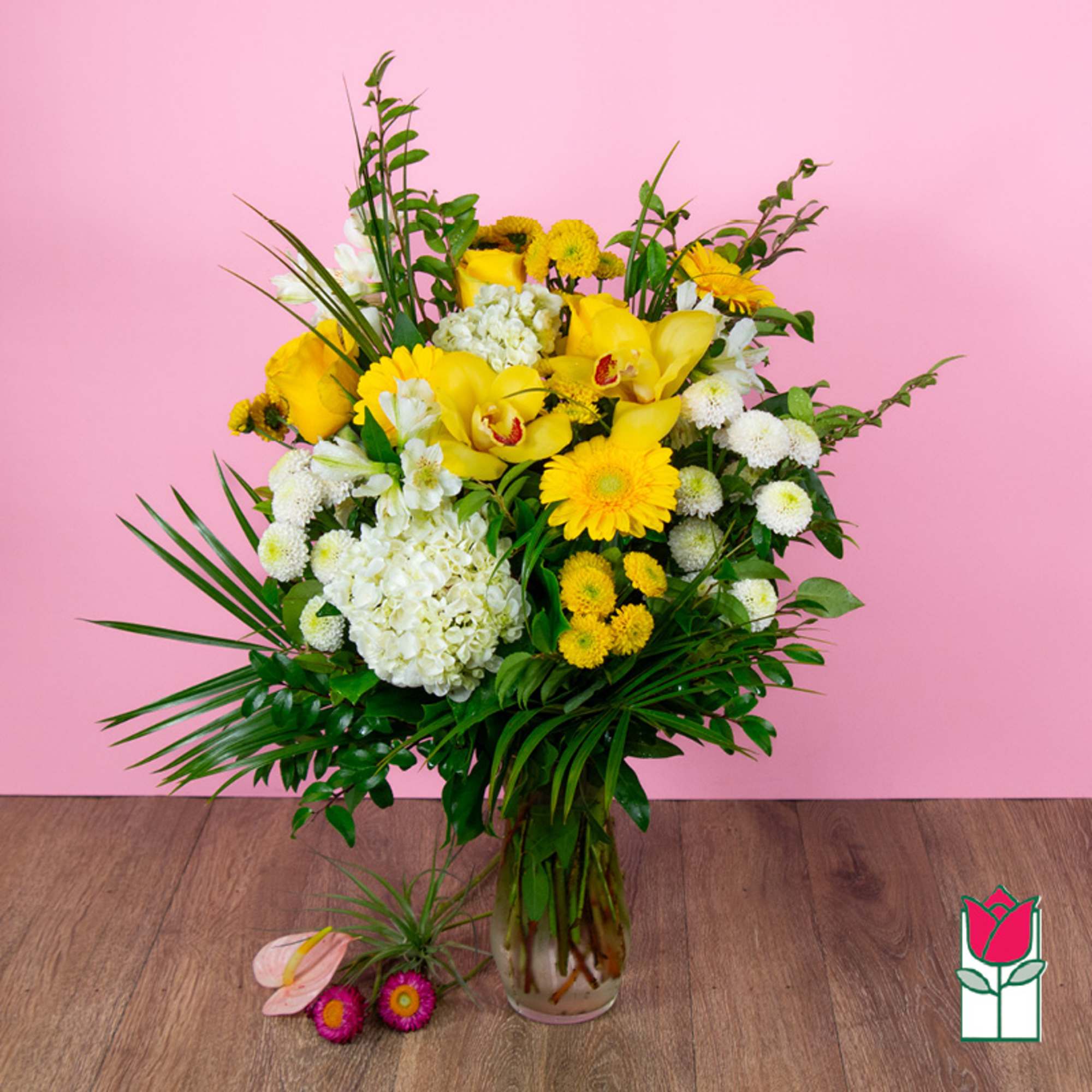 Yellow and white floral arrangement in a glass vase with tropical leaves