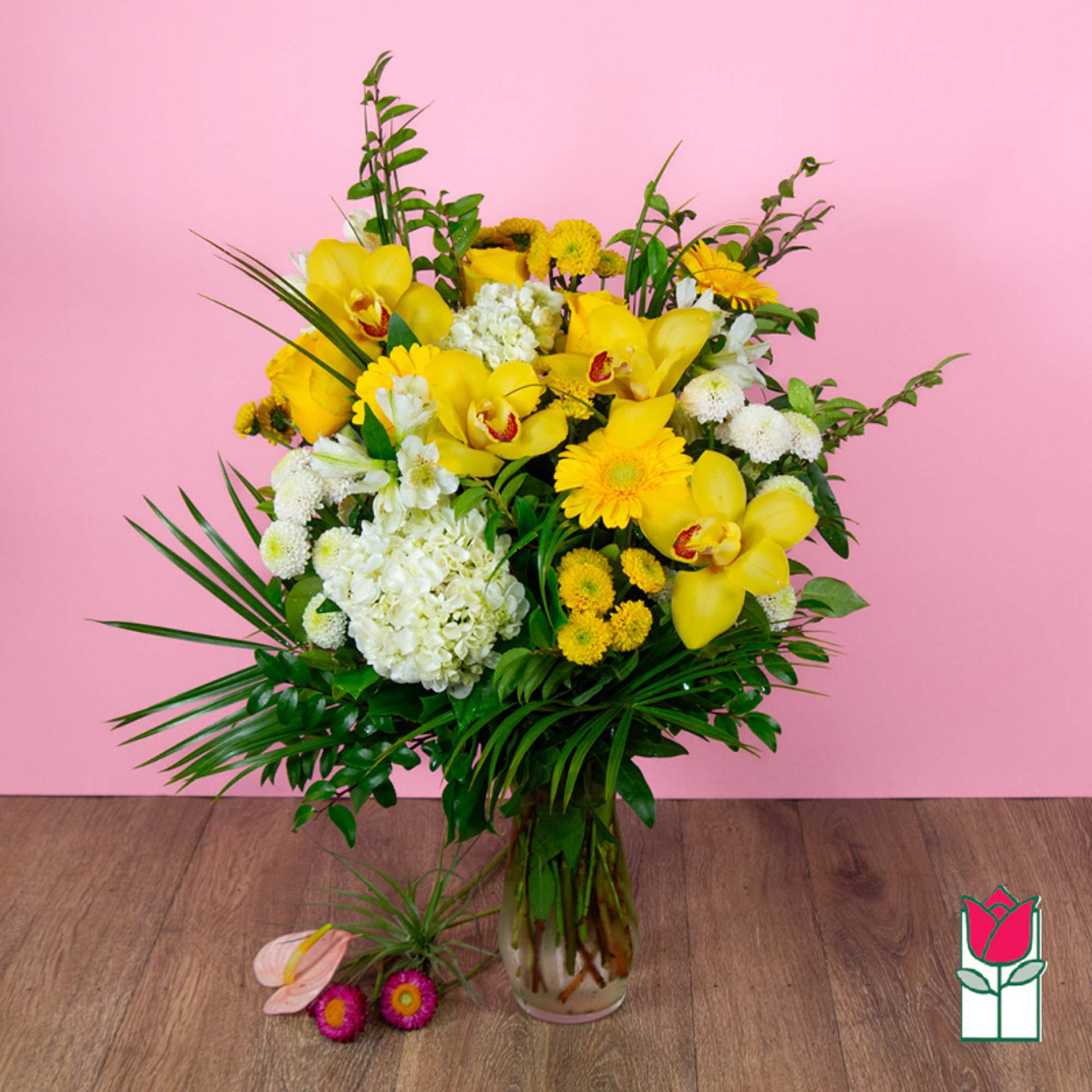 Yellow and white floral arrangement in a glass vase with tropical greenery
