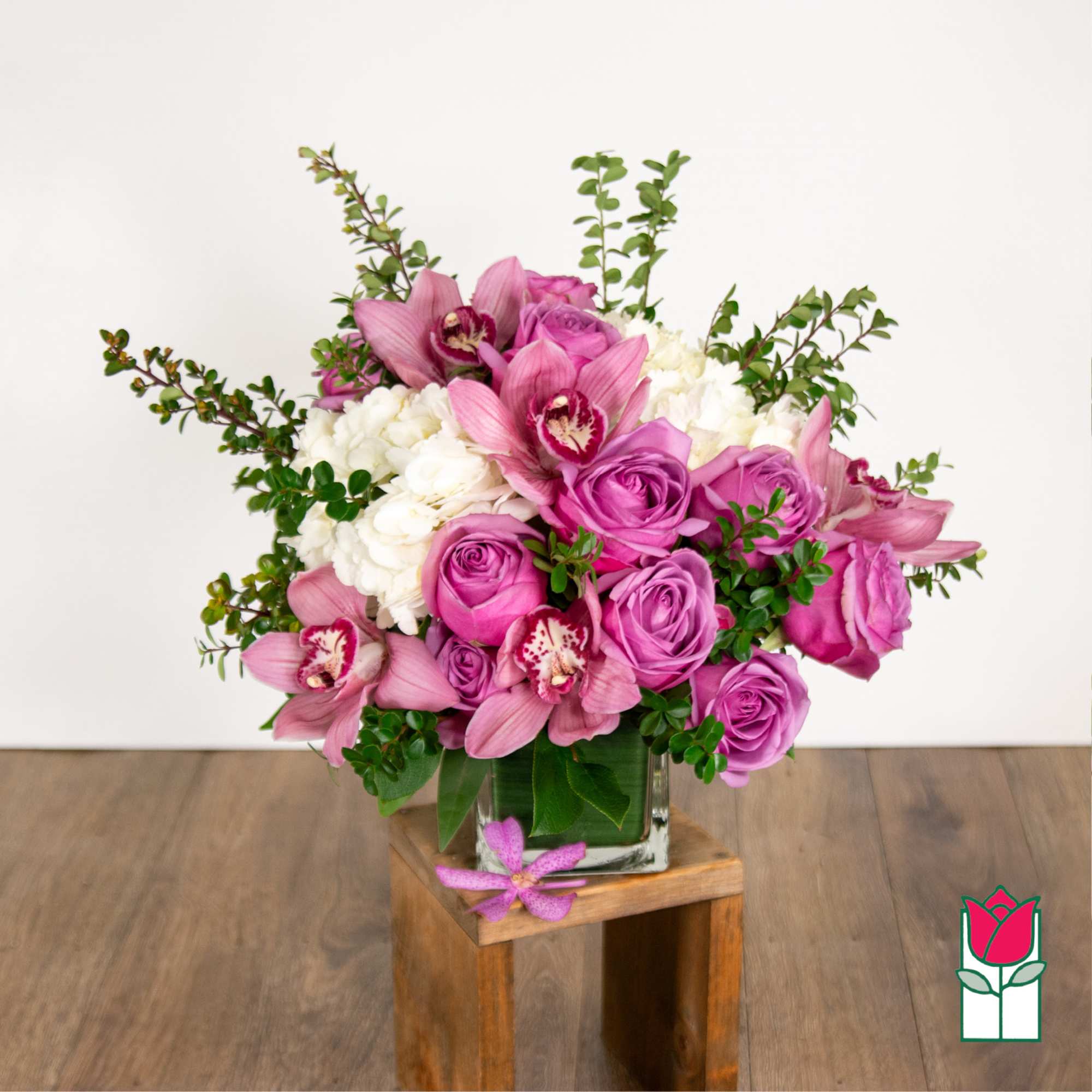 Pink and white floral arrangement in a glass vase on a wooden stand