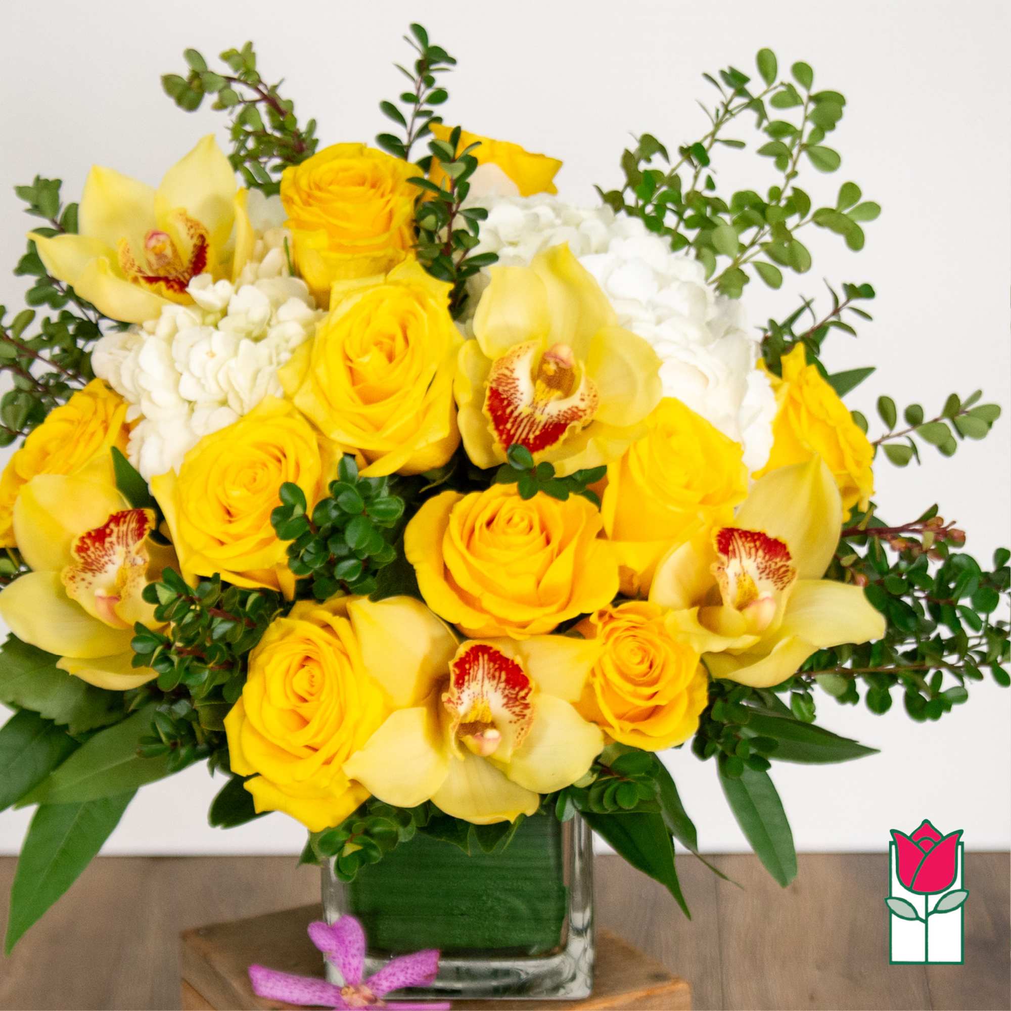 Yellow roses and orchids in a glass vase with greenery