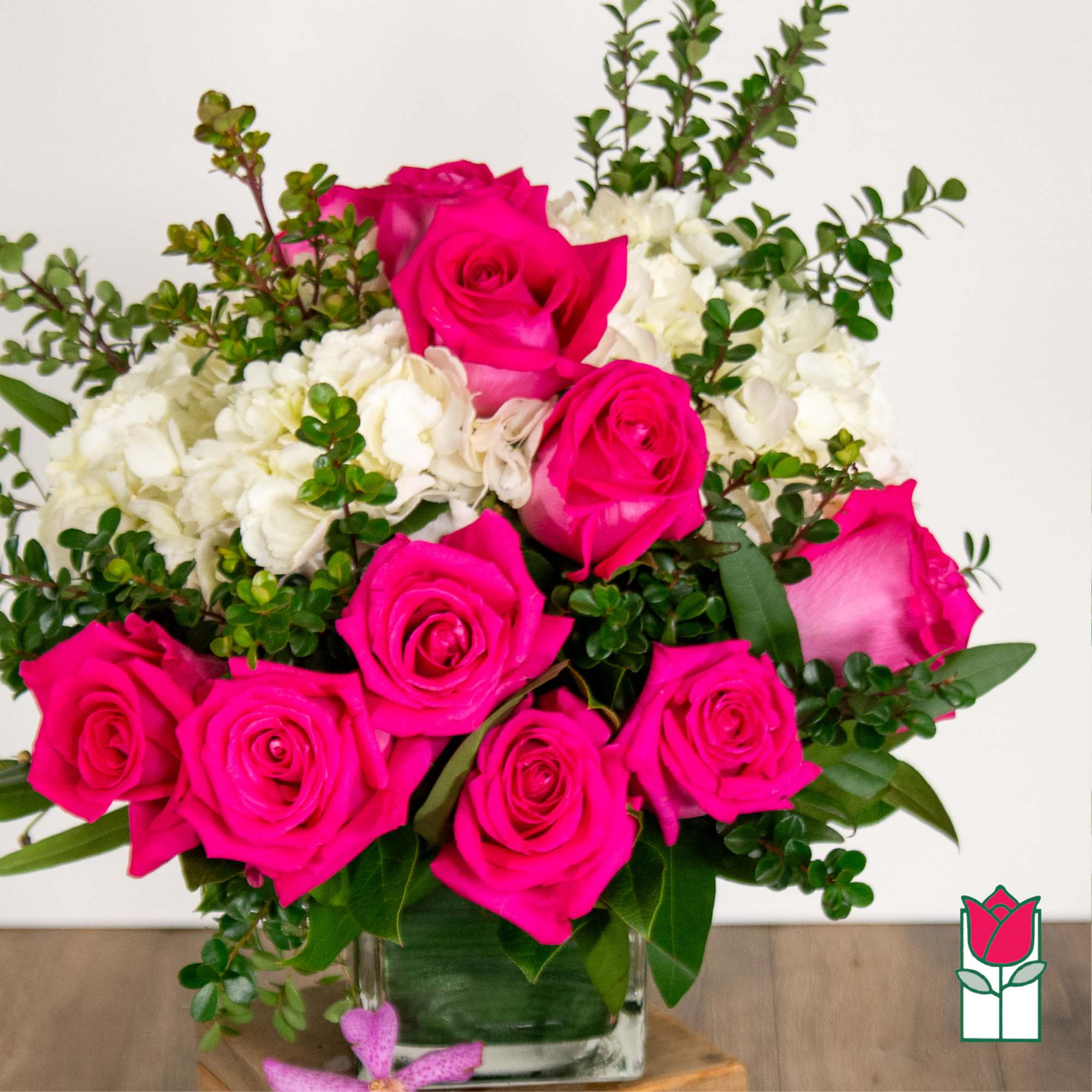 Hot pink roses arranged with white flowers in a clear glass vase