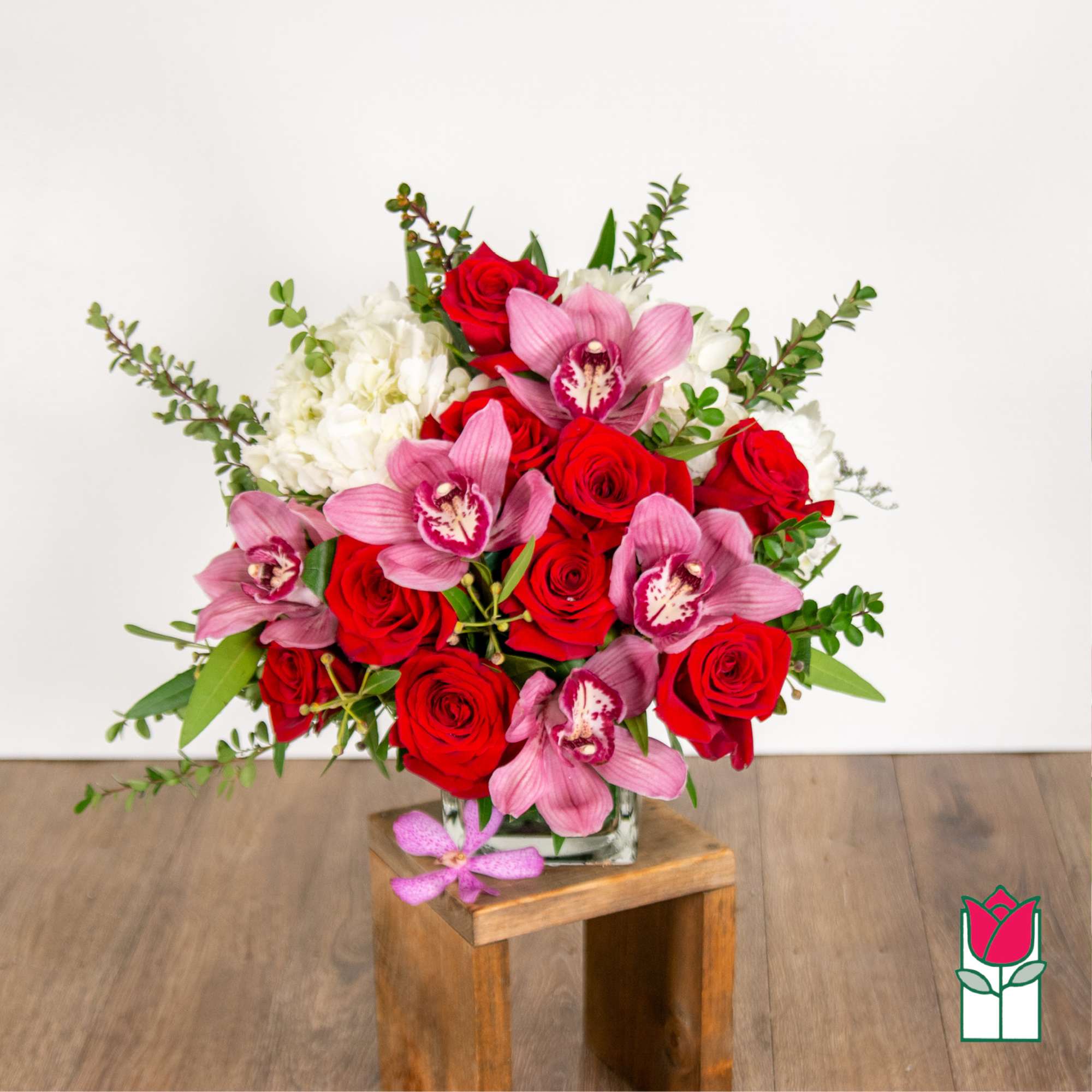 Bouquet of red roses, pink orchids, and white hydrangeas in a glass vase