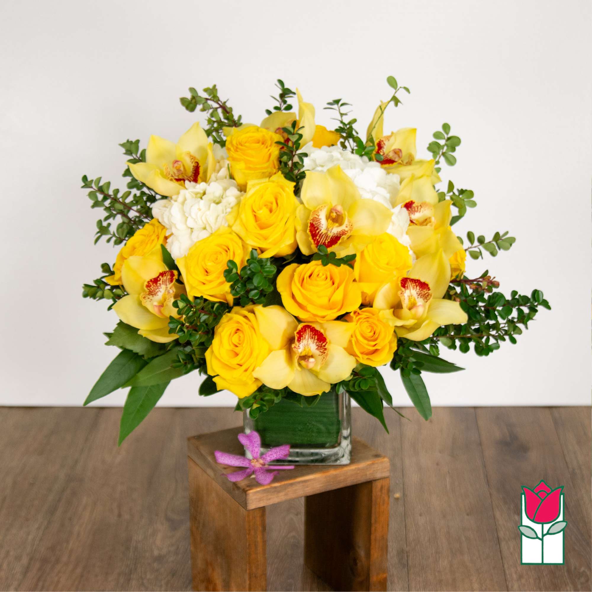 Yellow roses and orchids arranged in a clear glass vase