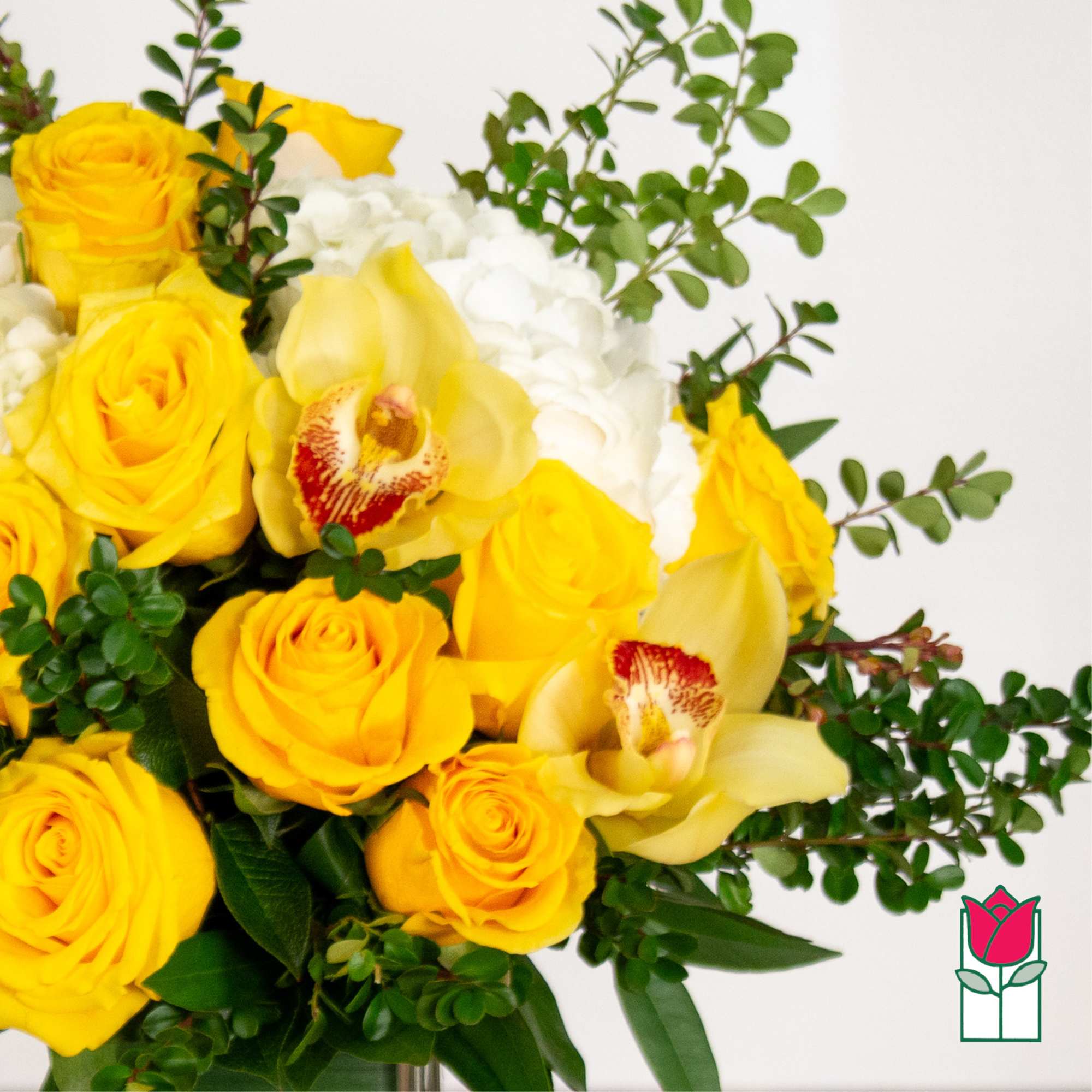 Yellow roses and orchids arranged with white blooms in a vase
