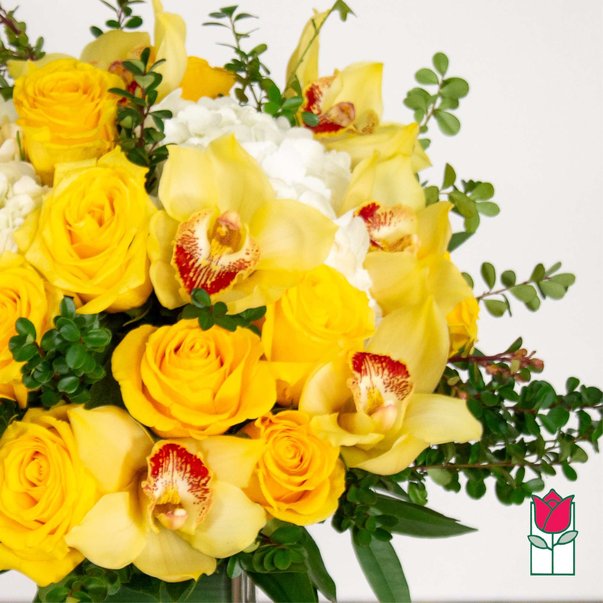 Yellow roses and orchids arranged with white blooms in a vase