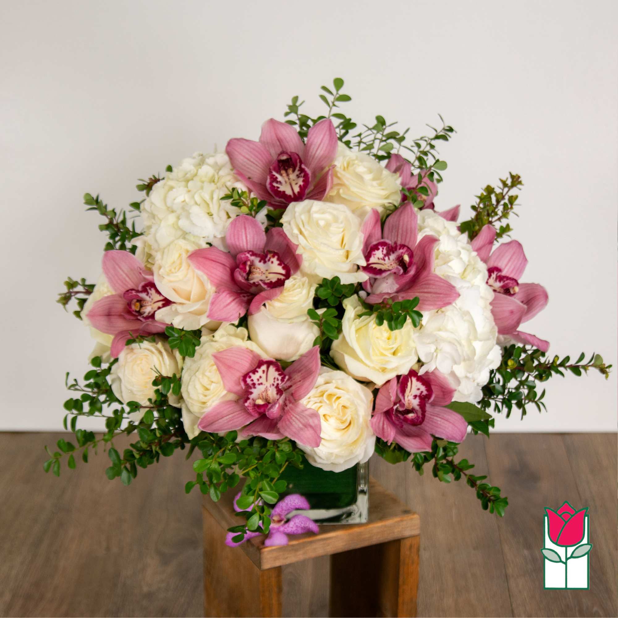 Pink orchids and white roses arranged in a square glass vase