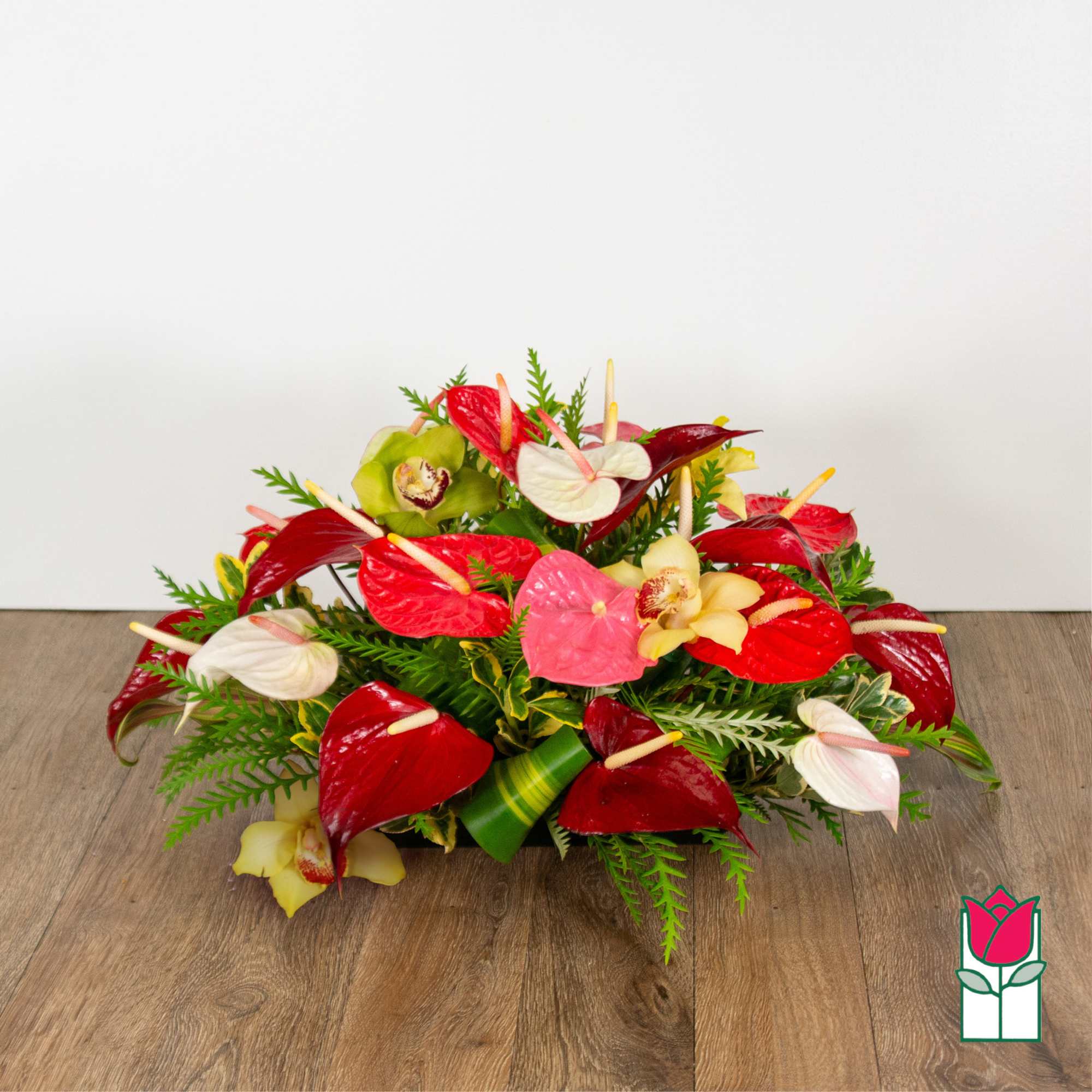 Low arrangement of red, white, pink, and yellow anthuriums with orchids