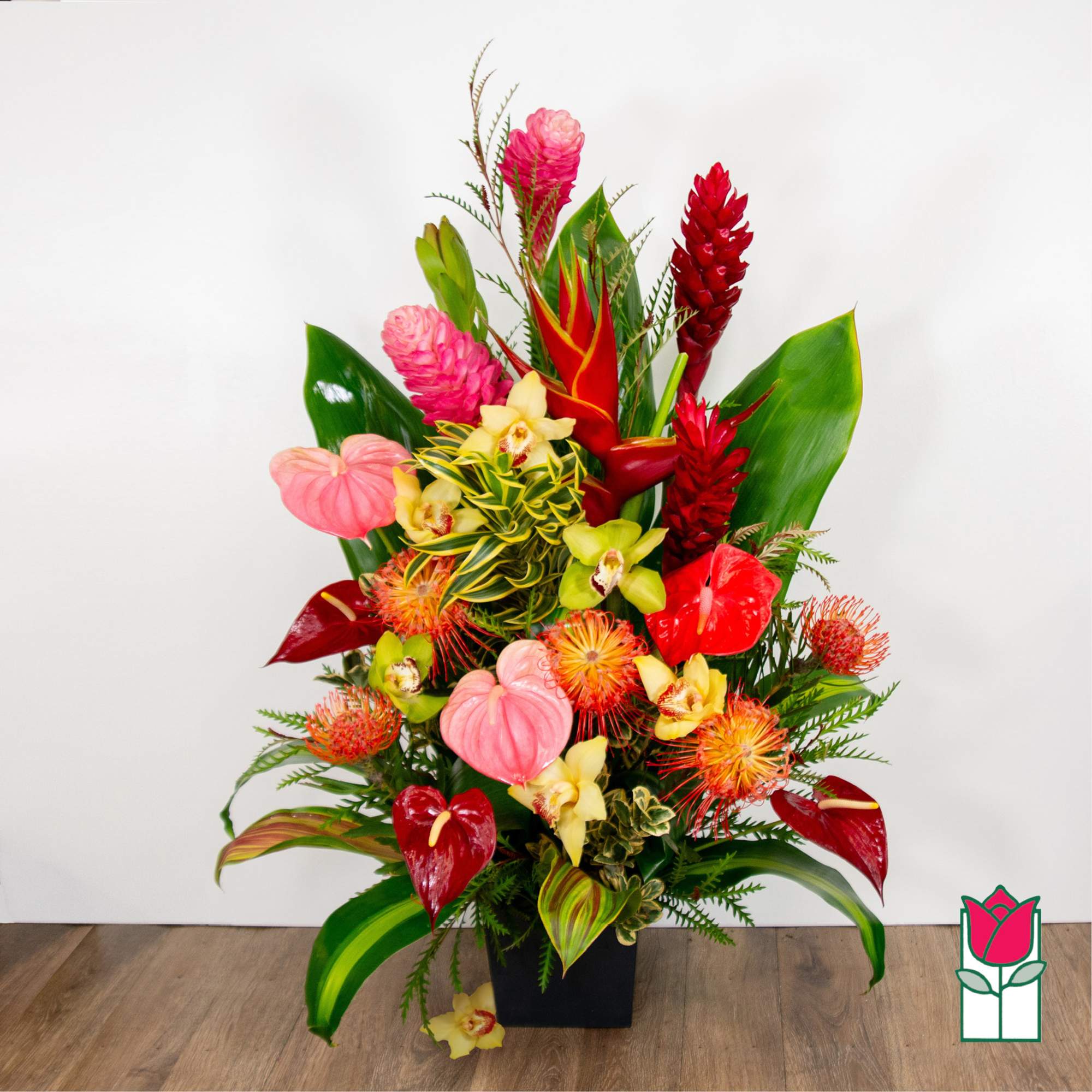 Tropical flower arrangement with red, pink, and yellow blooms in a black vase