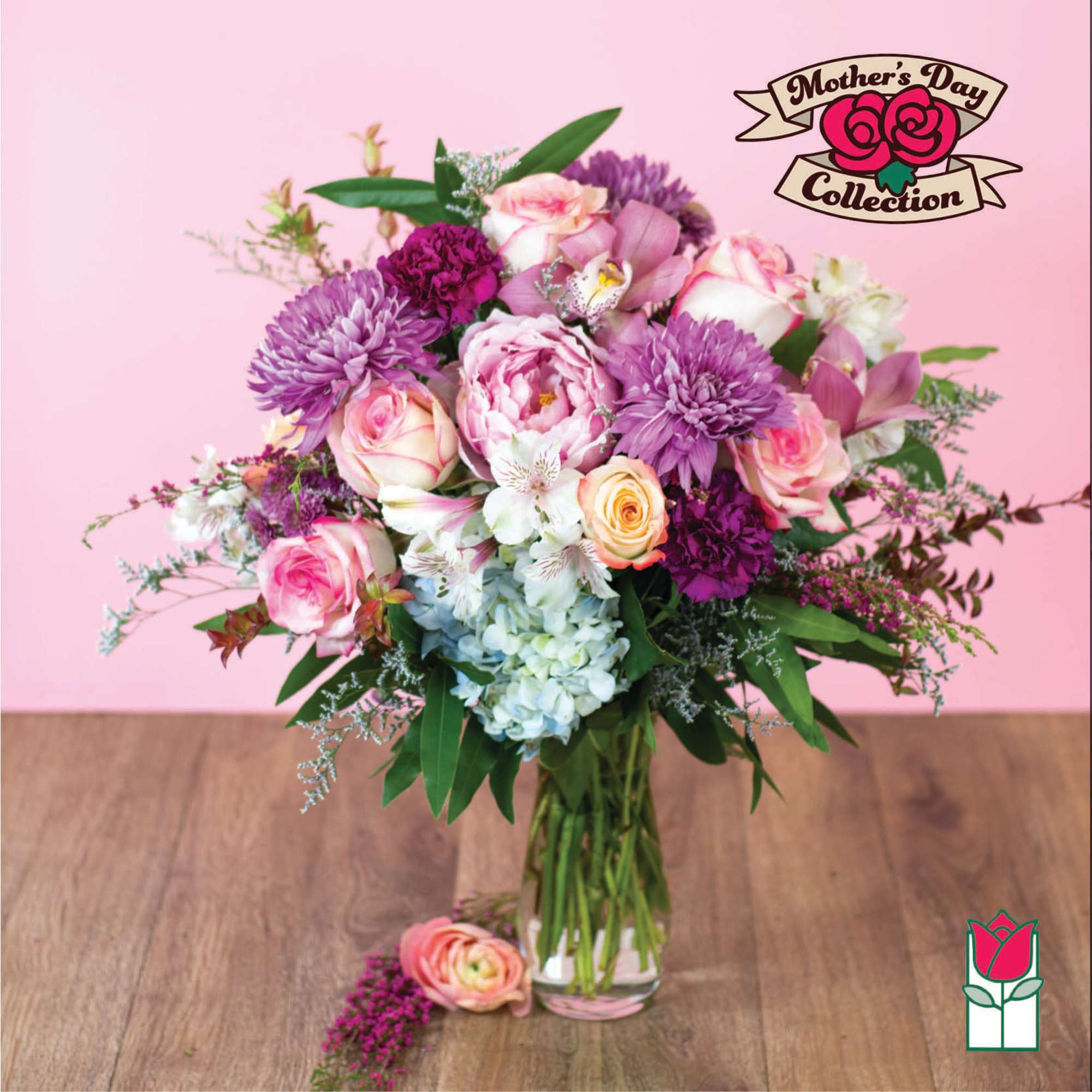 Pink and purple mixed flower arrangement with roses and hydrangeas in a clear glass vase on a wood table.