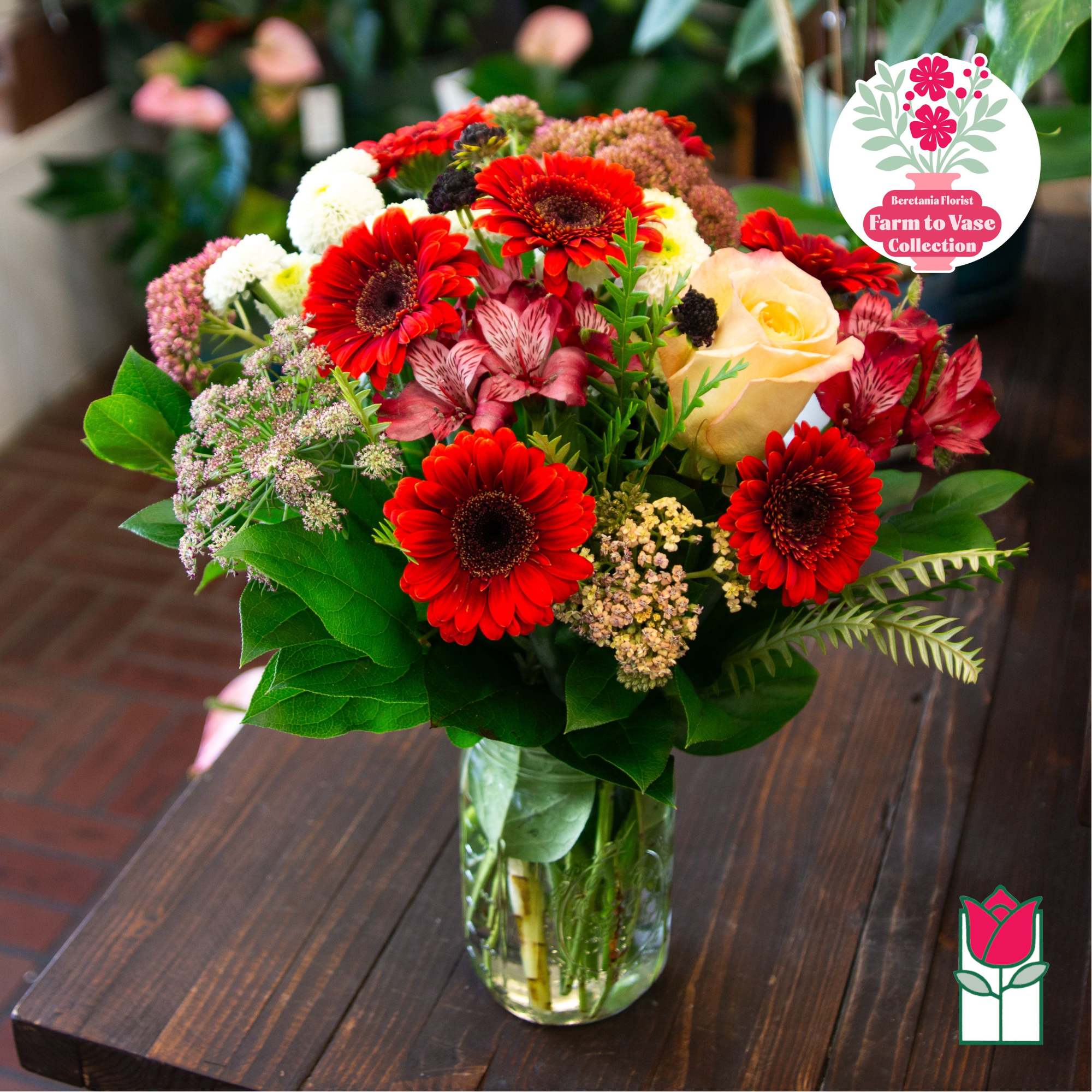 Mixed bouquet of red gerbera daisies and a pale rose in a glass vase