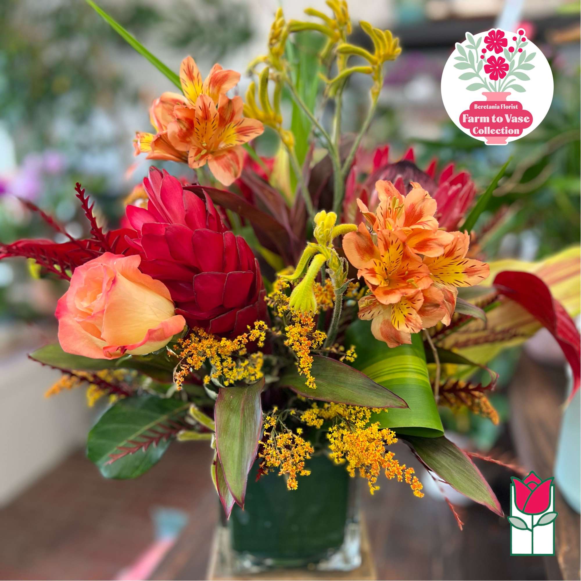 Tropical bouquet with orange alstroemeria, red rose, and yellow filler in a glass vase