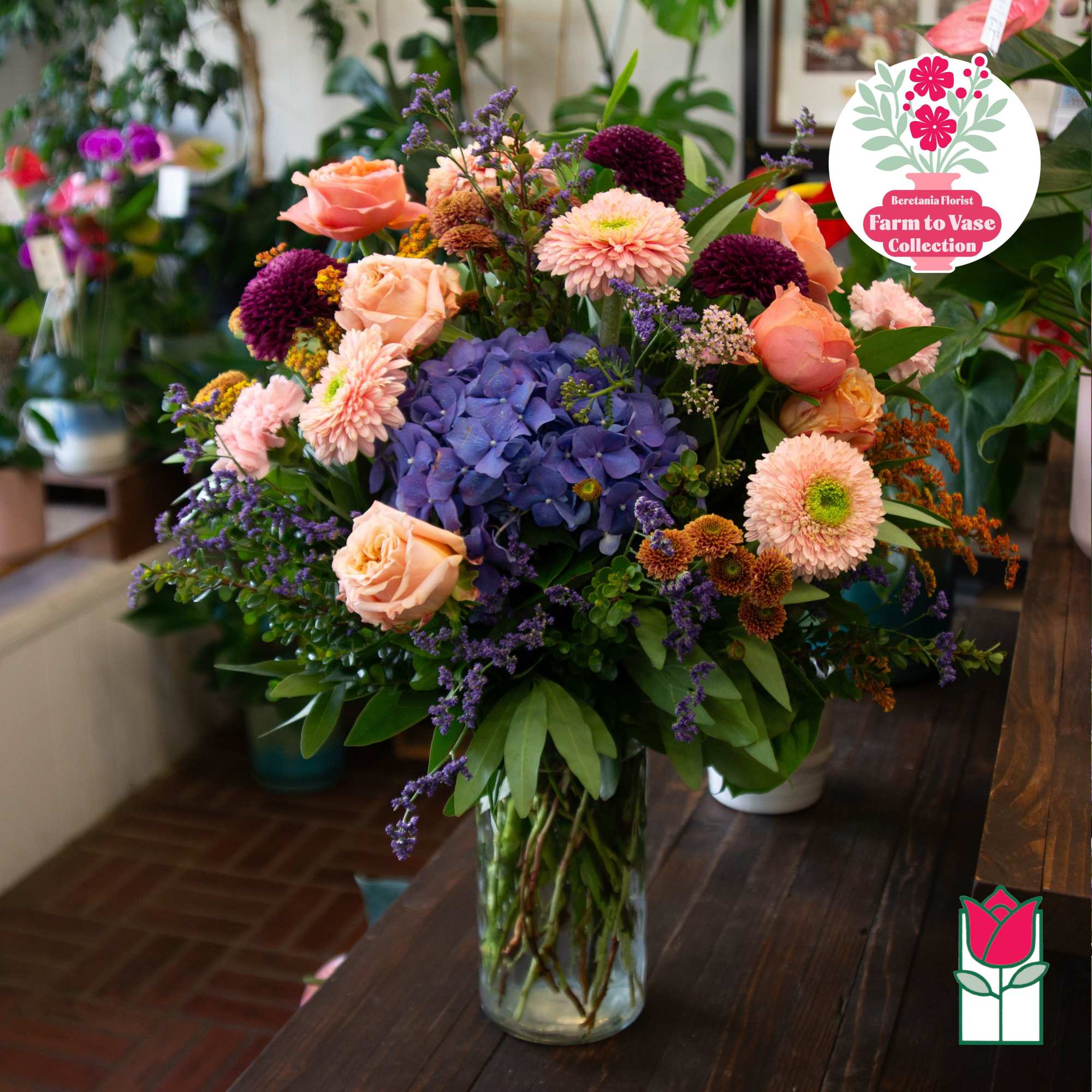 Mixed bouquet of peach roses, purple blooms, and blue hydrangea in a glass vase
