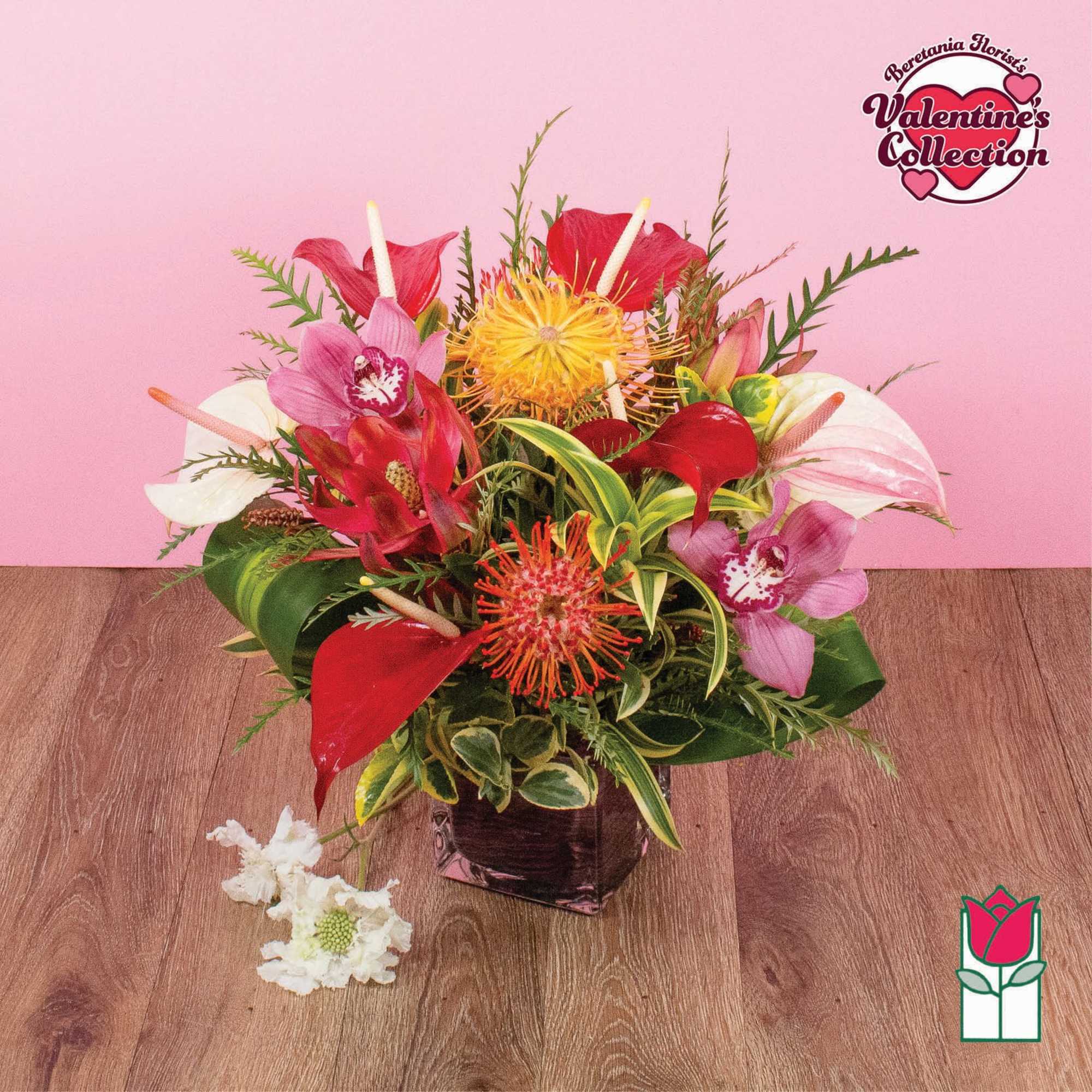 Tropical arrangement of red anthuriums, pink orchids, and orange protea in a dark glass cube vase