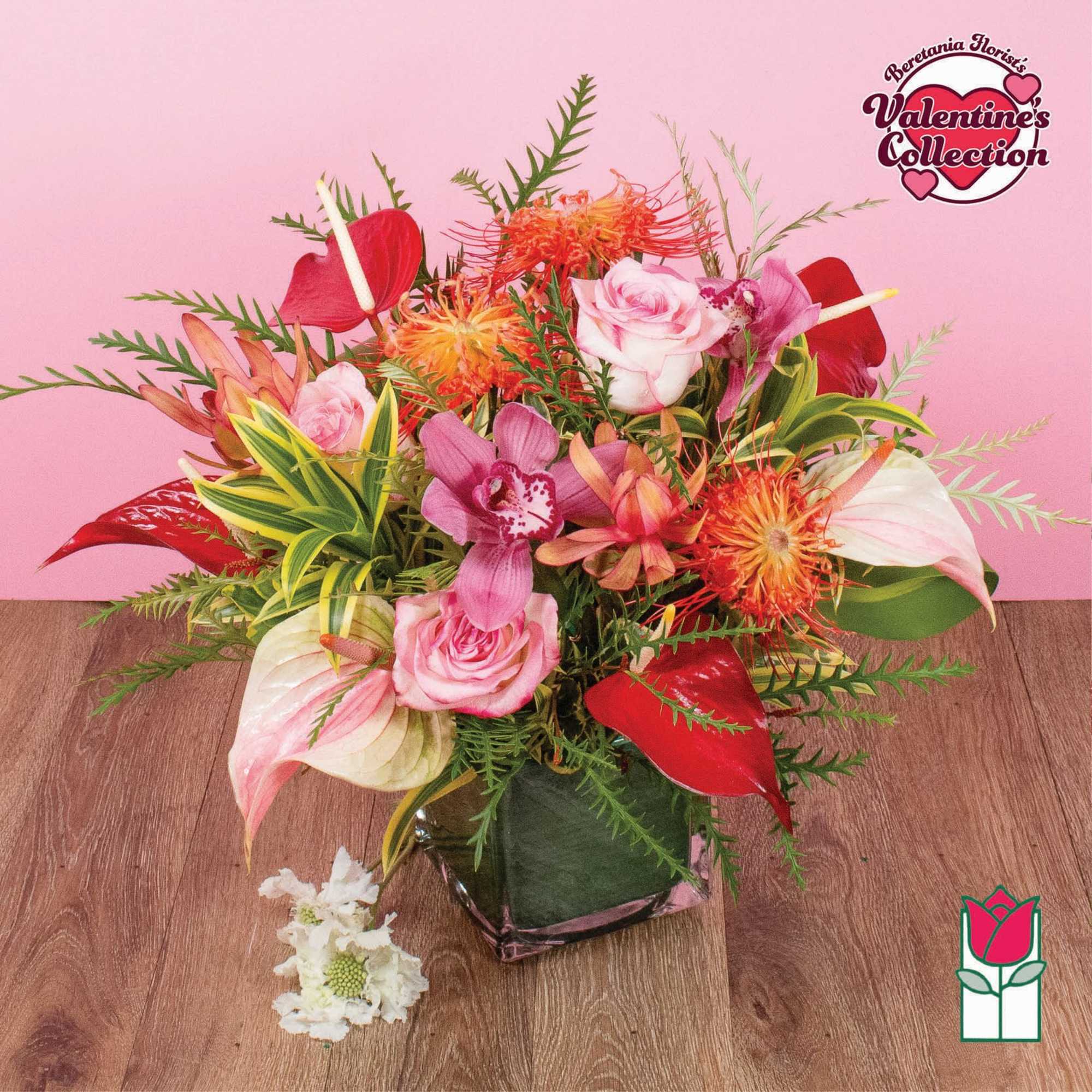 Mixed arrangement of pink roses, orchids, and tropical blooms in a glass cube vase