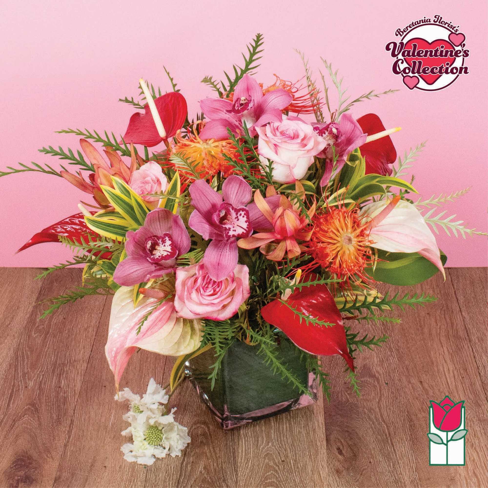 Pink roses and orchids with red anthurium and orange protea in a square glass vase