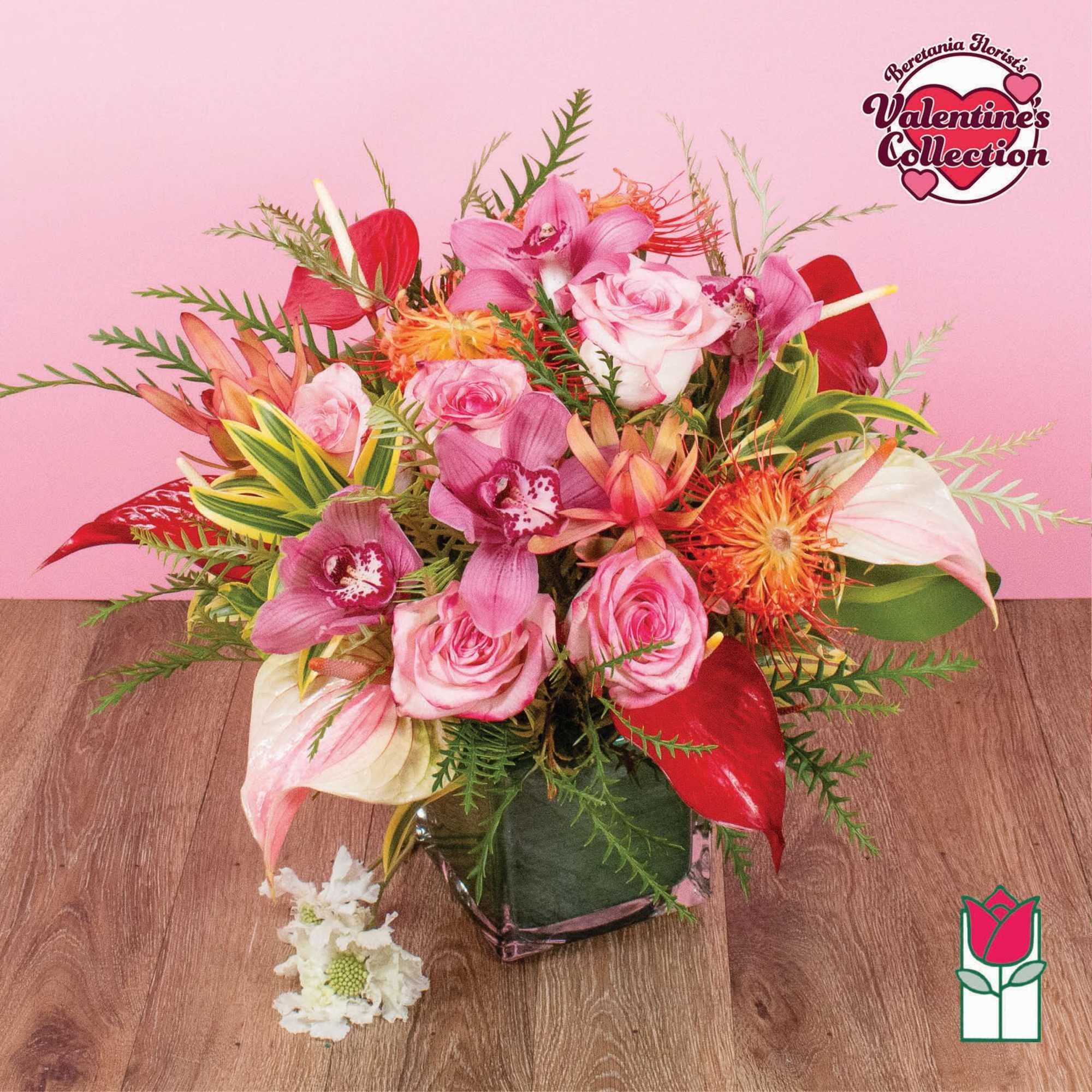 Mixed pink roses and orchids with red tropical flowers in a clear glass cube vase