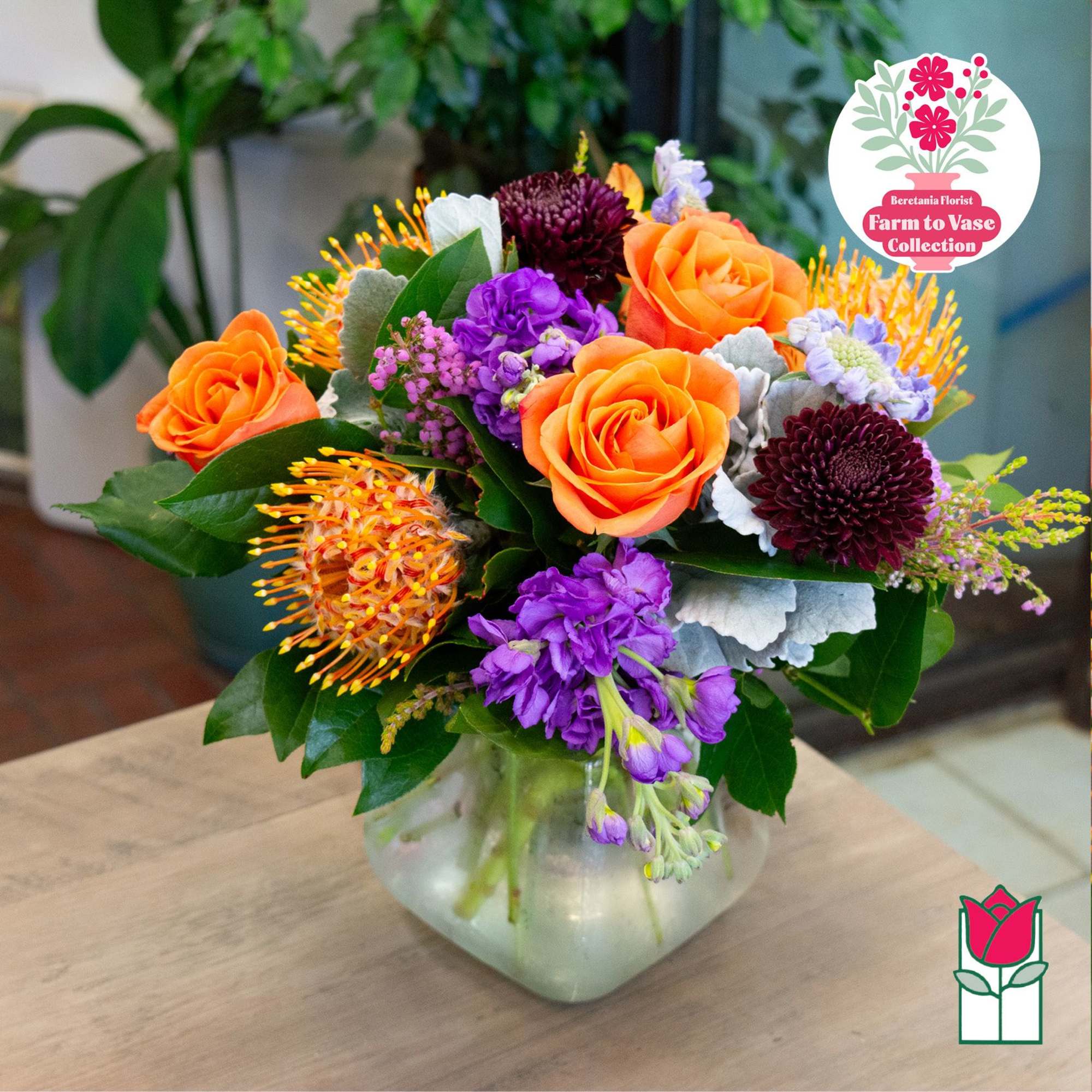 Mixed bouquet of orange roses and purple flowers in a glass vase