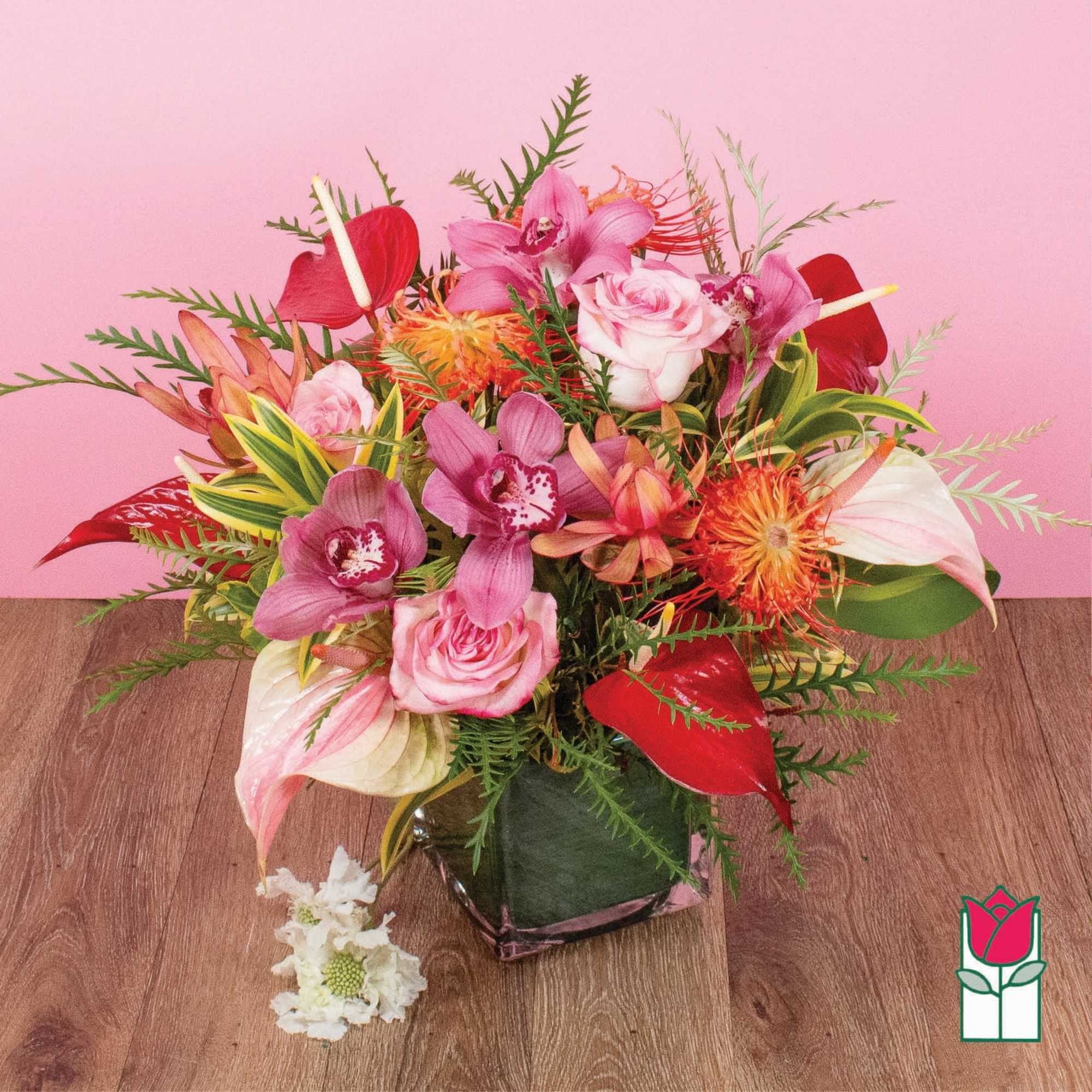 Tropical arrangement of pink orchids, roses, red anthurium and orange protea in a glass cube vase