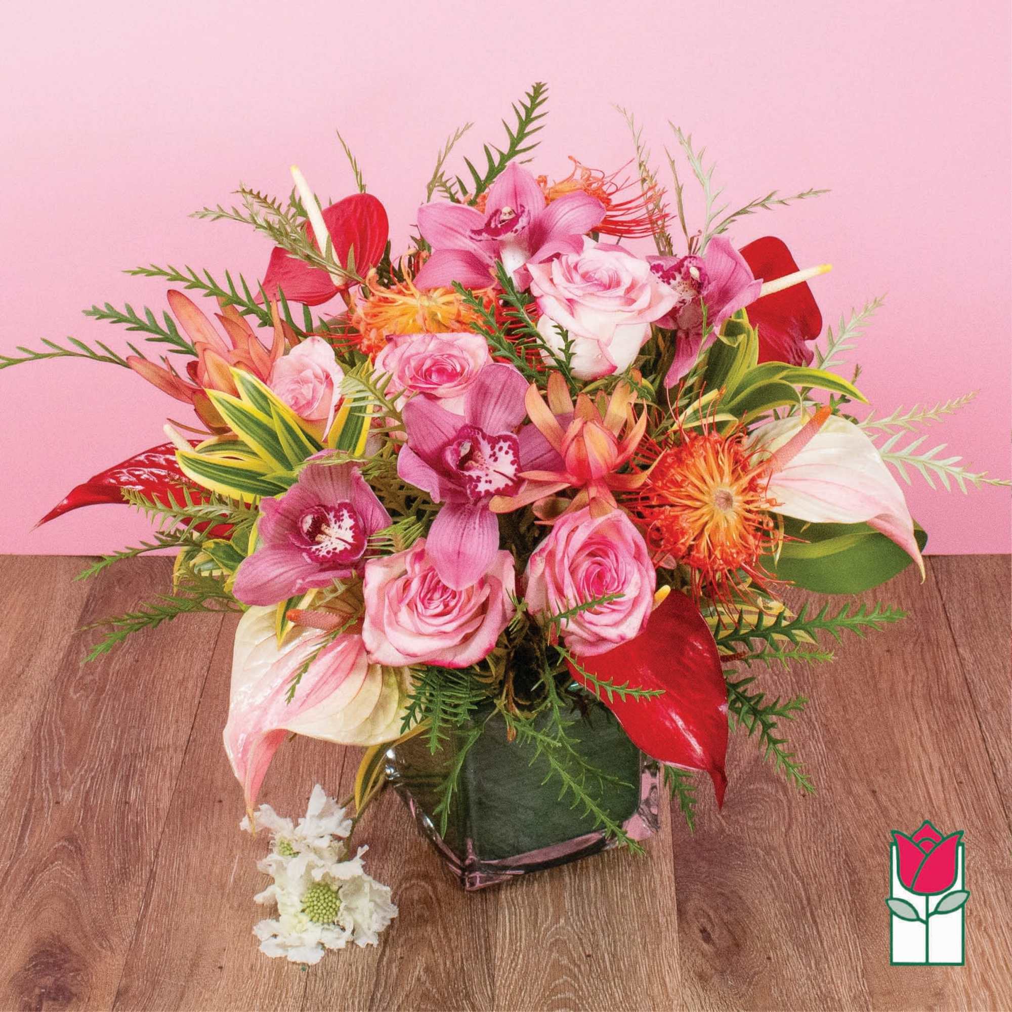 Mixed arrangement of pink roses, orchids, and tropical blooms in a square glass vase