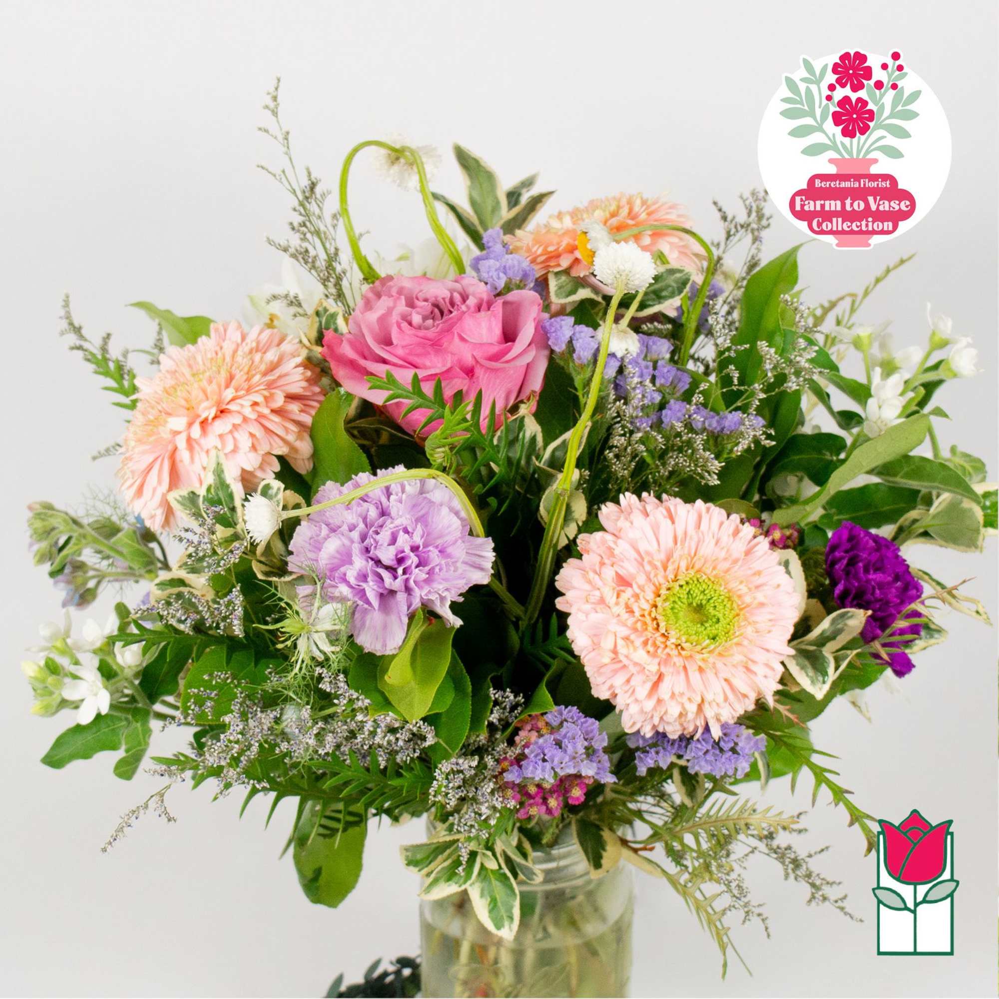 Mixed bouquet of pink, peach, purple, and white flowers in a glass vase