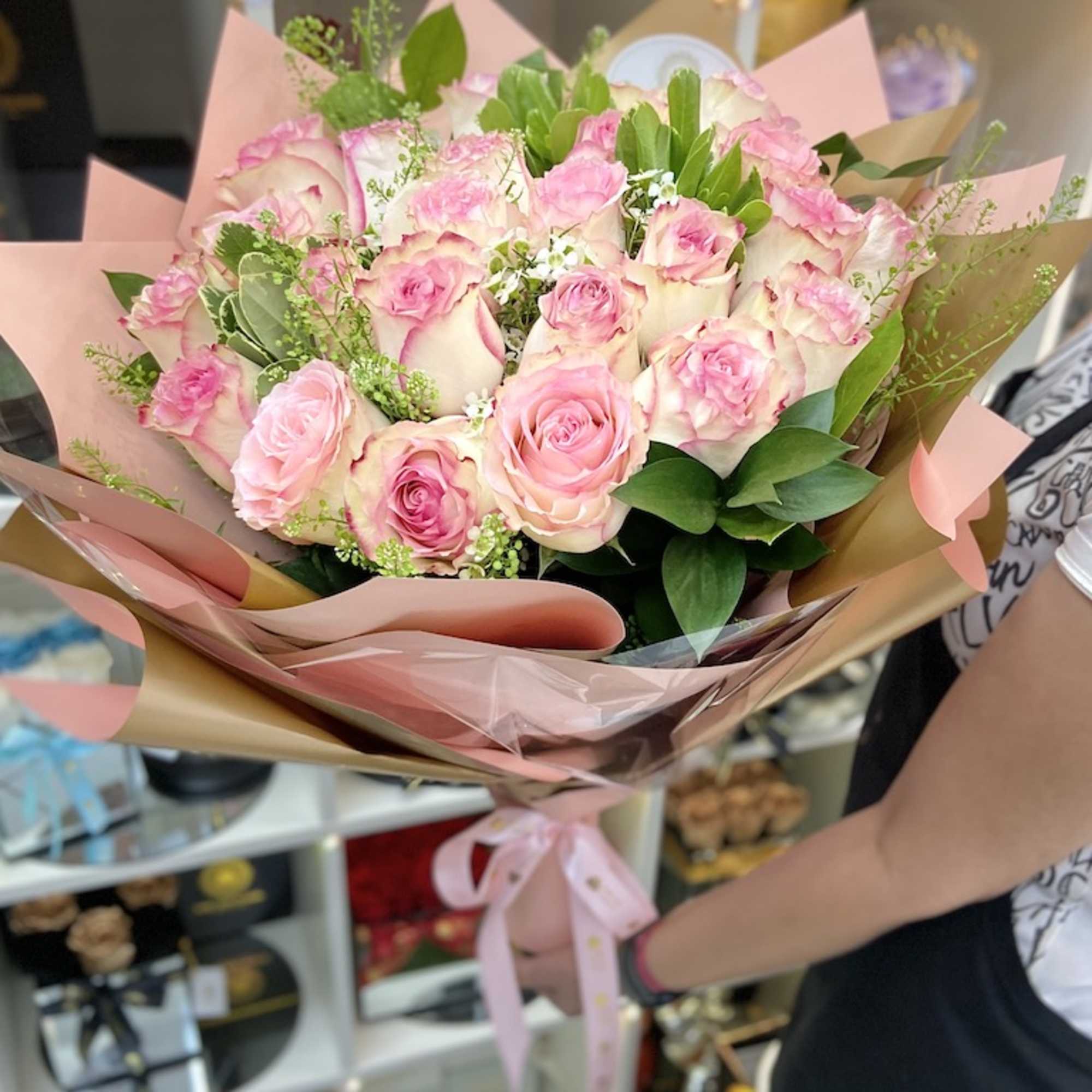 Large hand-tied bouquet of pink and white roses wrapped in pink paper with a satin ribbon bow.