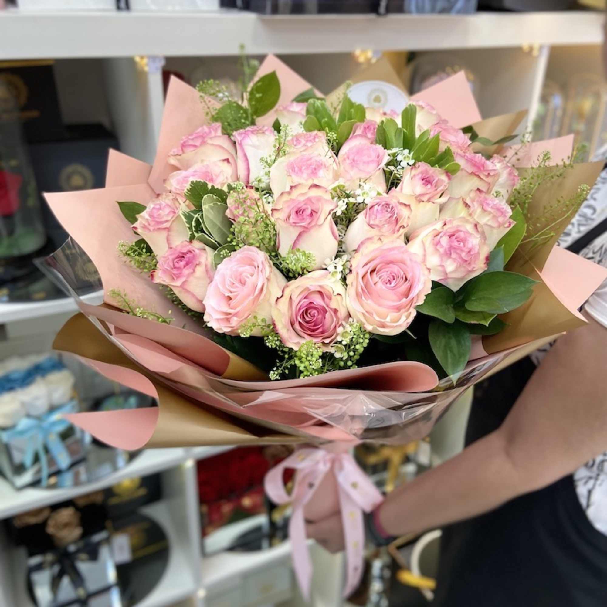 Large bouquet of pink roses wrapped in pink and gold paper with ribbon, held in a shop.