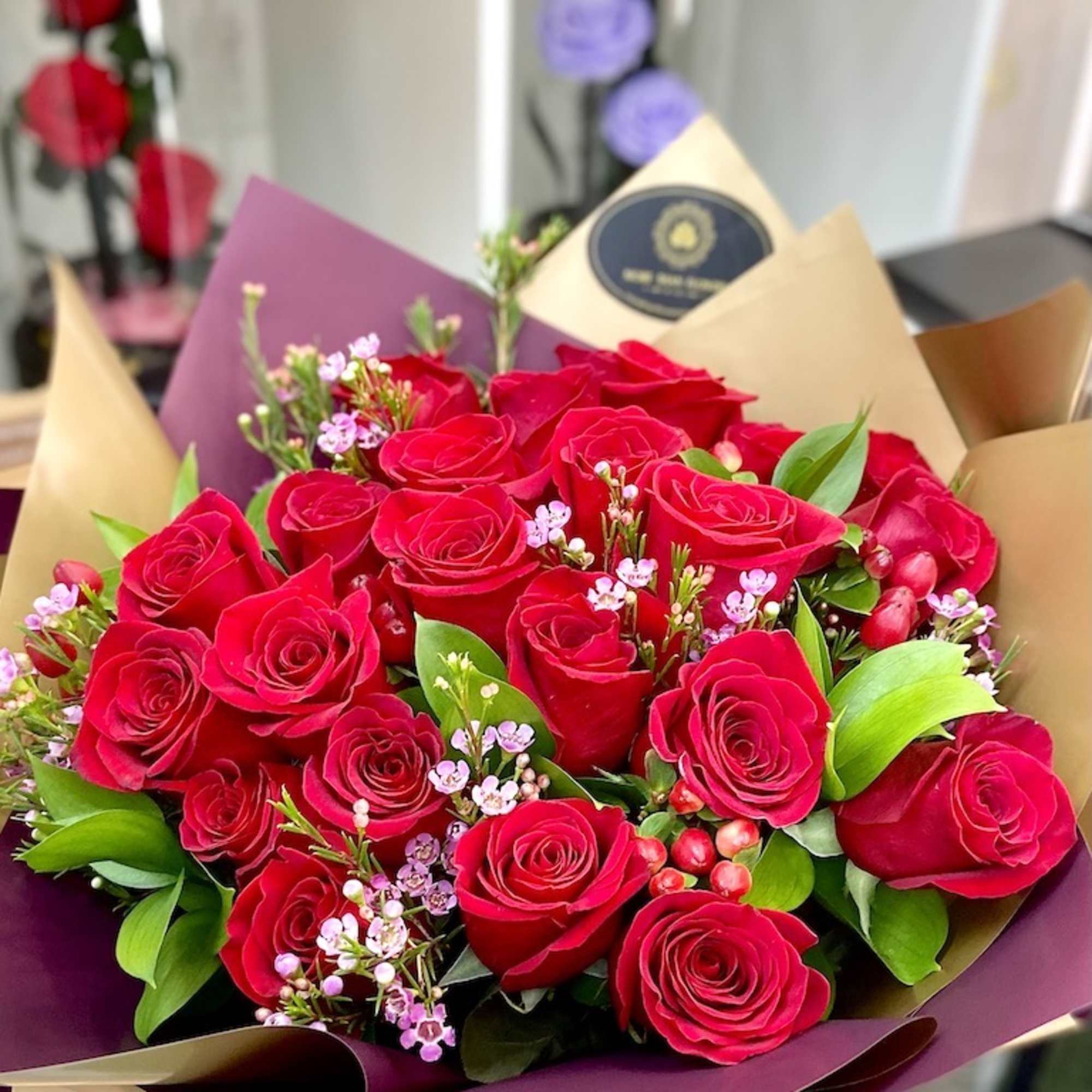 Large bouquet of red roses with small pink filler flowers wrapped in burgundy and tan paper