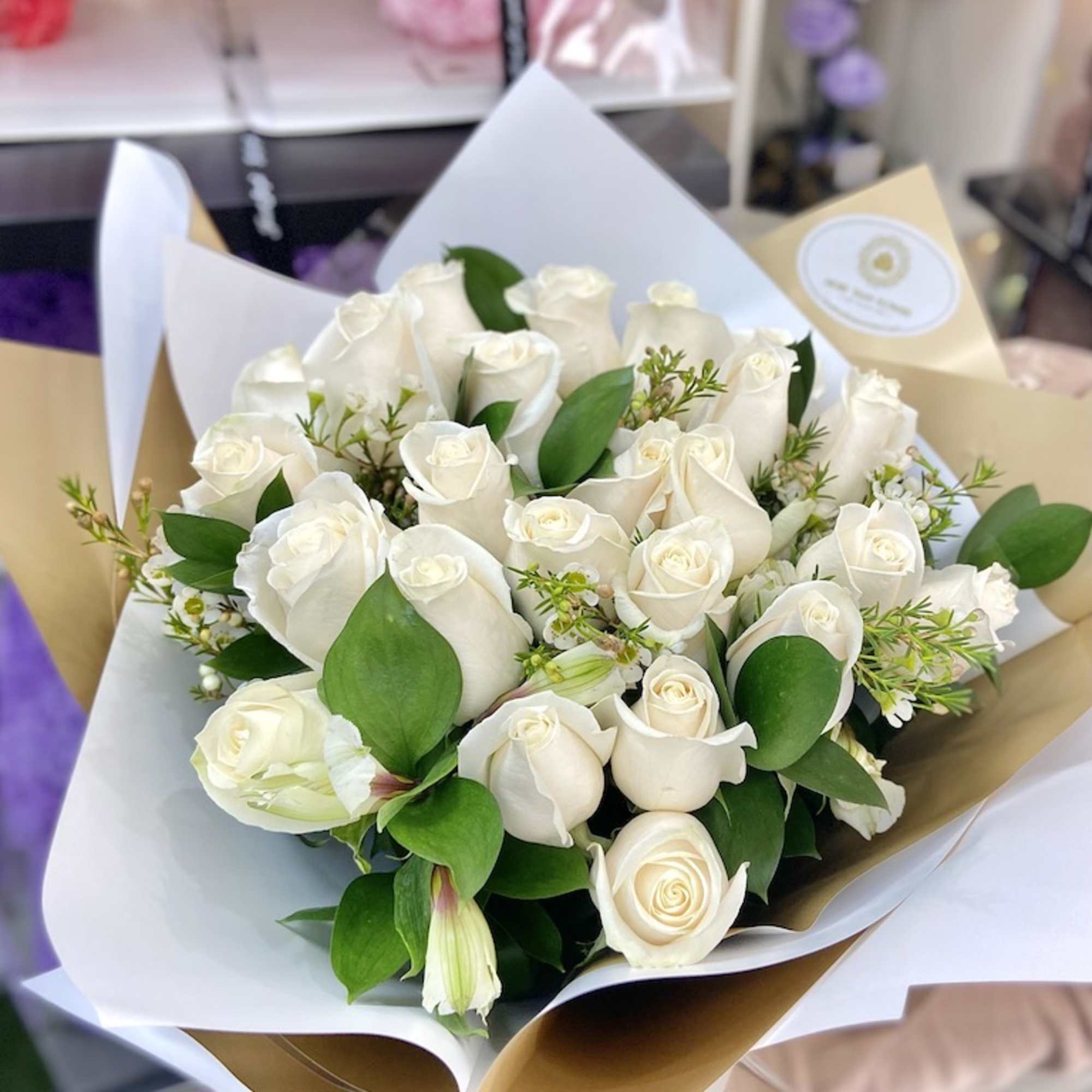 Handheld bouquet of white roses with green accents wrapped in layered white and tan paper