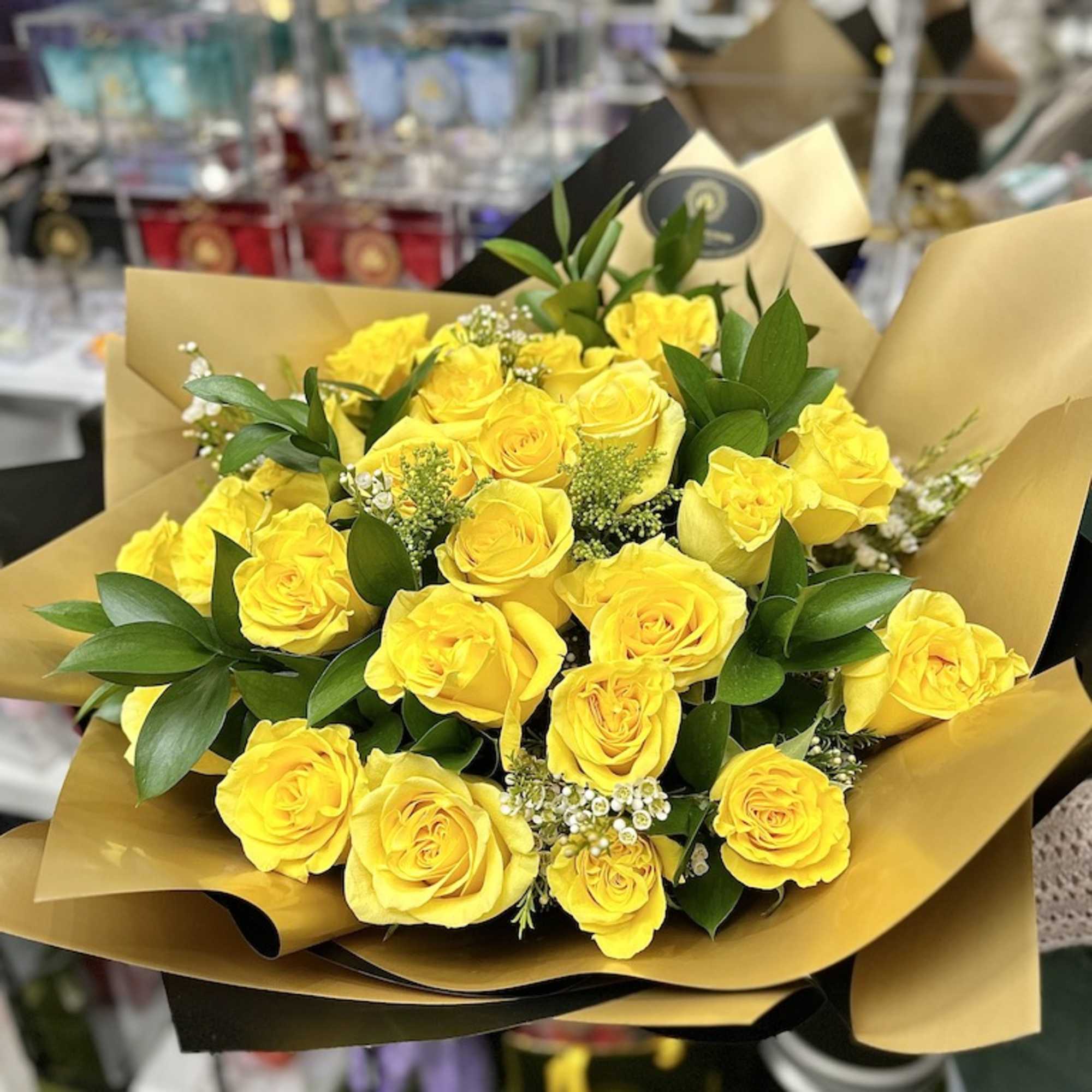 Hand-tied bouquet of bright yellow roses wrapped in gold and black paper.