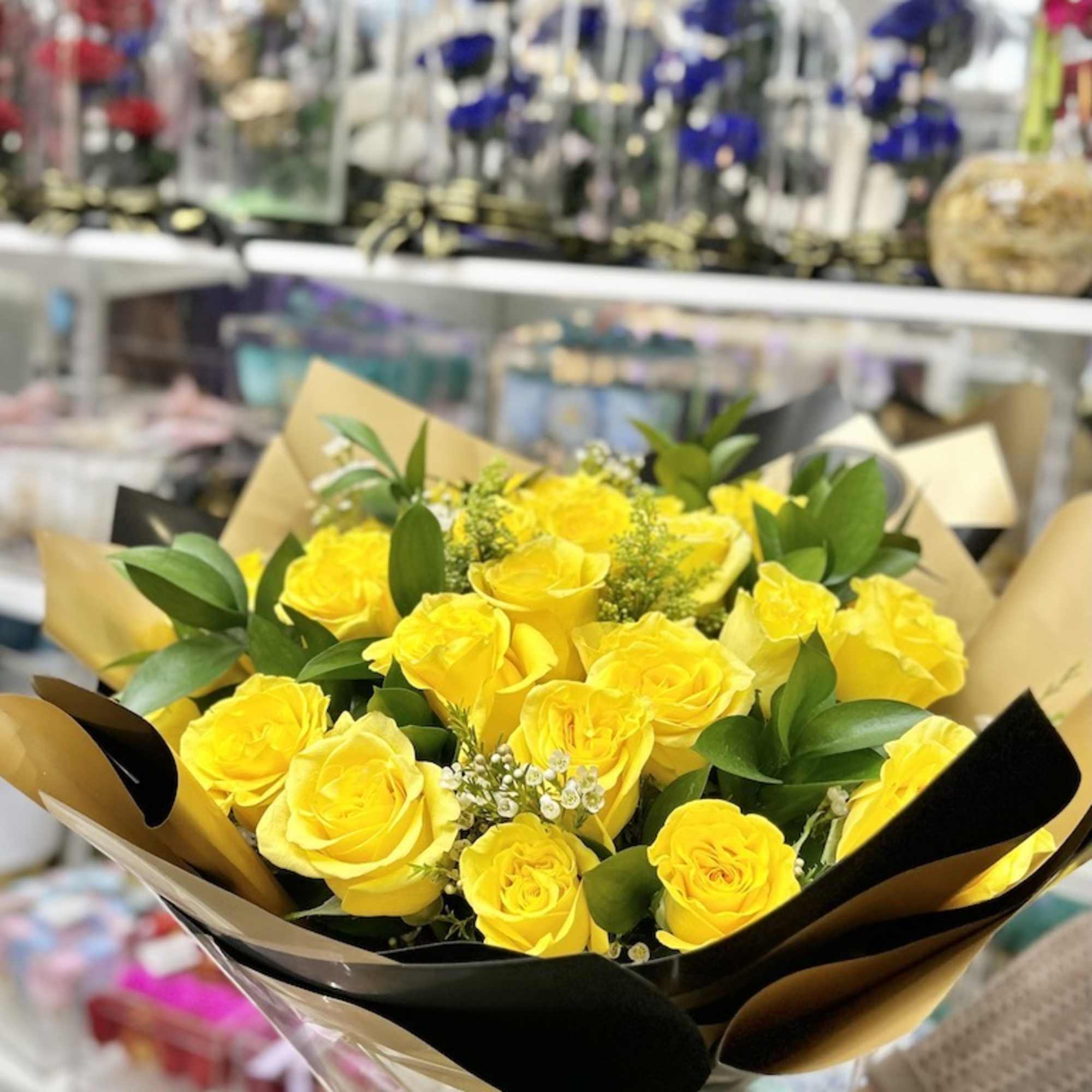 Bouquet of bright yellow roses with small white filler flowers wrapped in black and gold paper