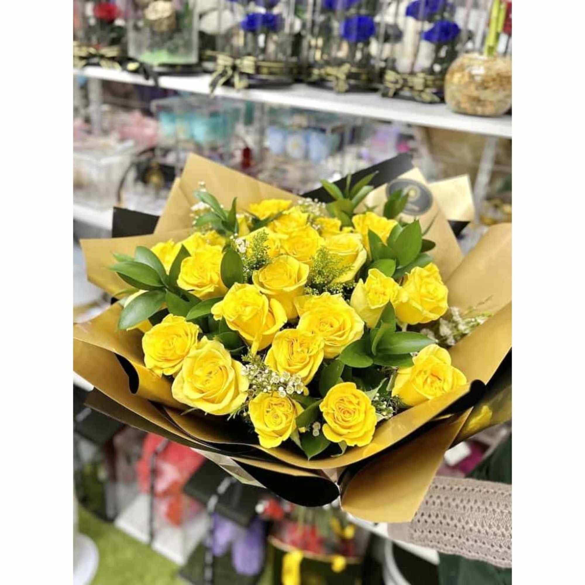 Hand-tied bouquet of bright yellow roses with filler flowers wrapped in brown and black paper