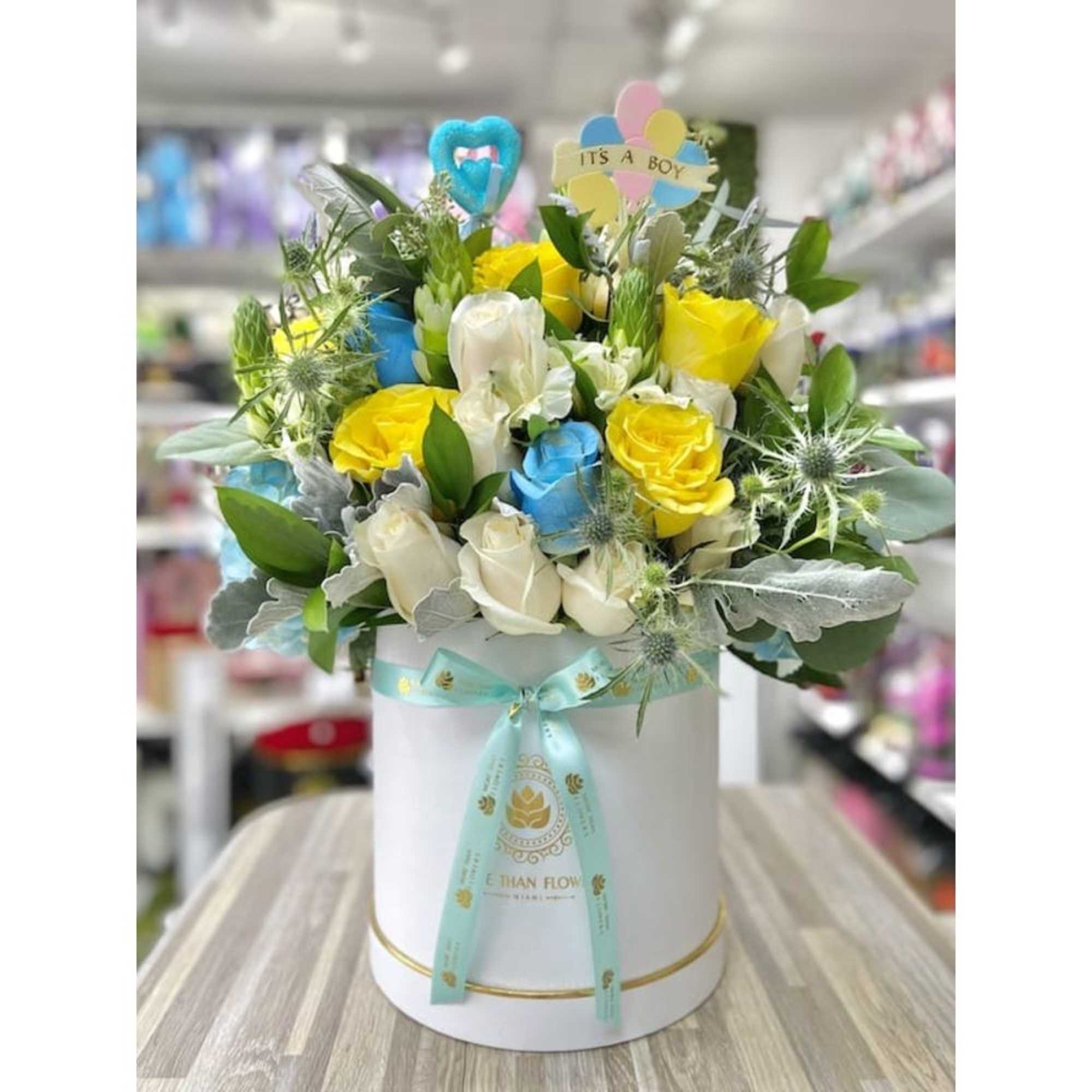 Round white hat box with yellow, blue, and white roses and an 'It's a Boy' pick
