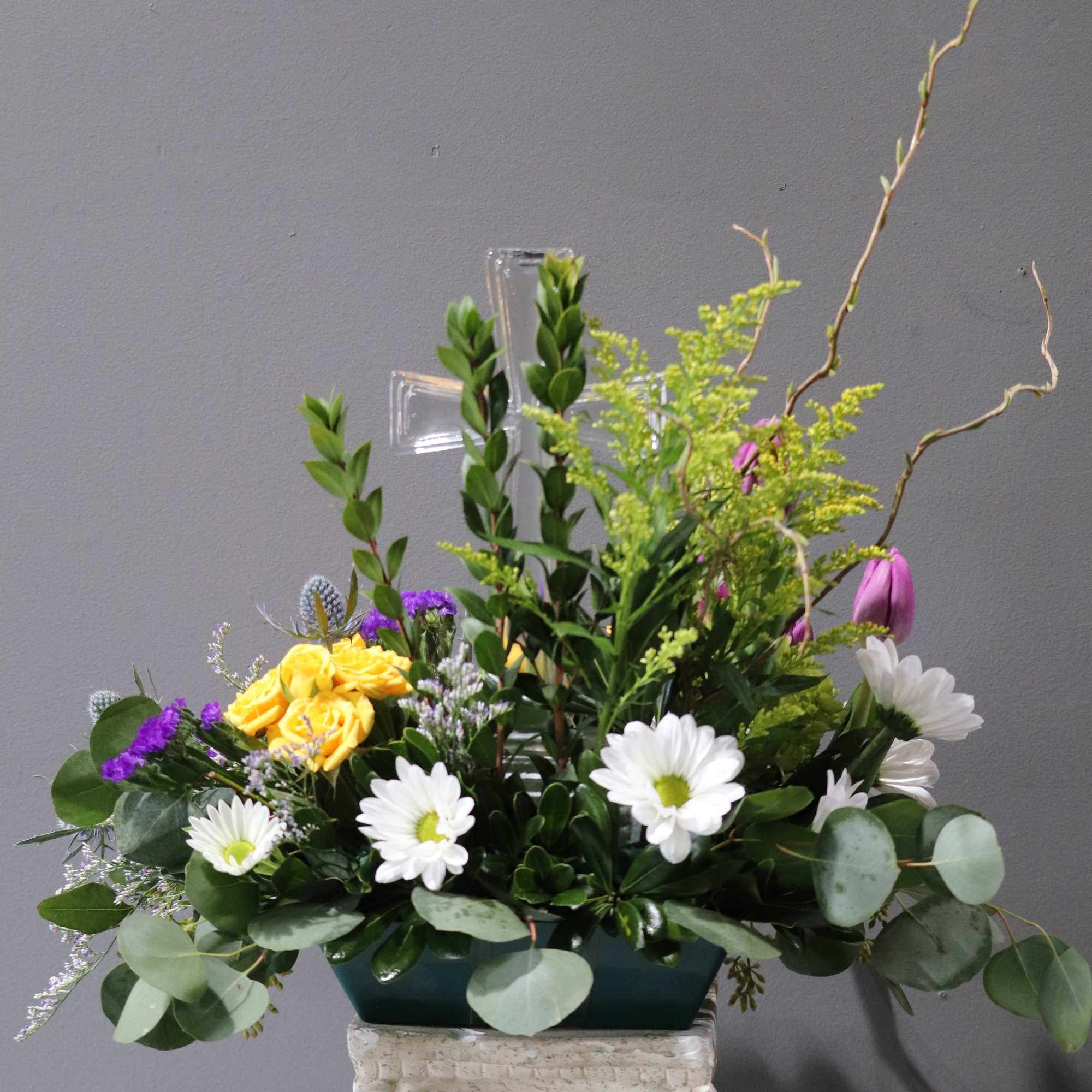 Mixed floral arrangement with yellow roses, white daisies, and purple accents in a rectangular vase