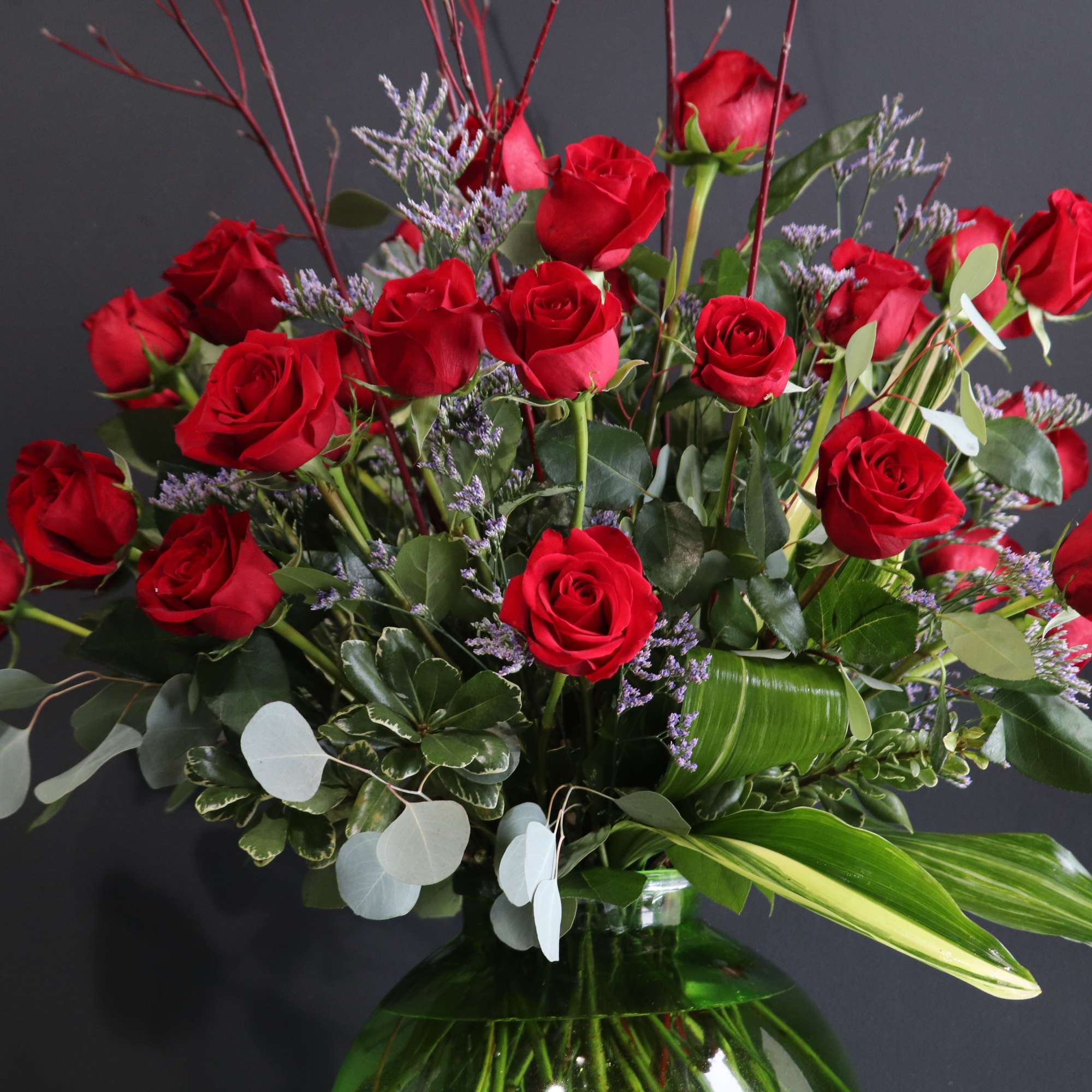 Red roses arranged in a green glass vase with mixed foliage