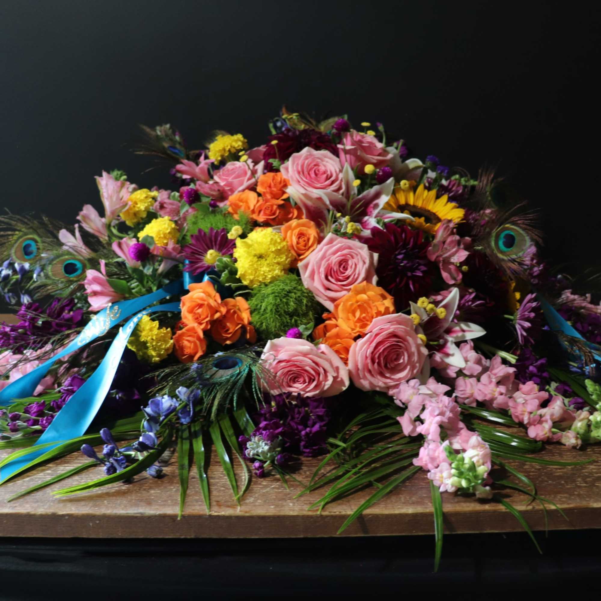 Colorful floral arrangement with roses, sunflowers, and peacock feathers on a wooden table