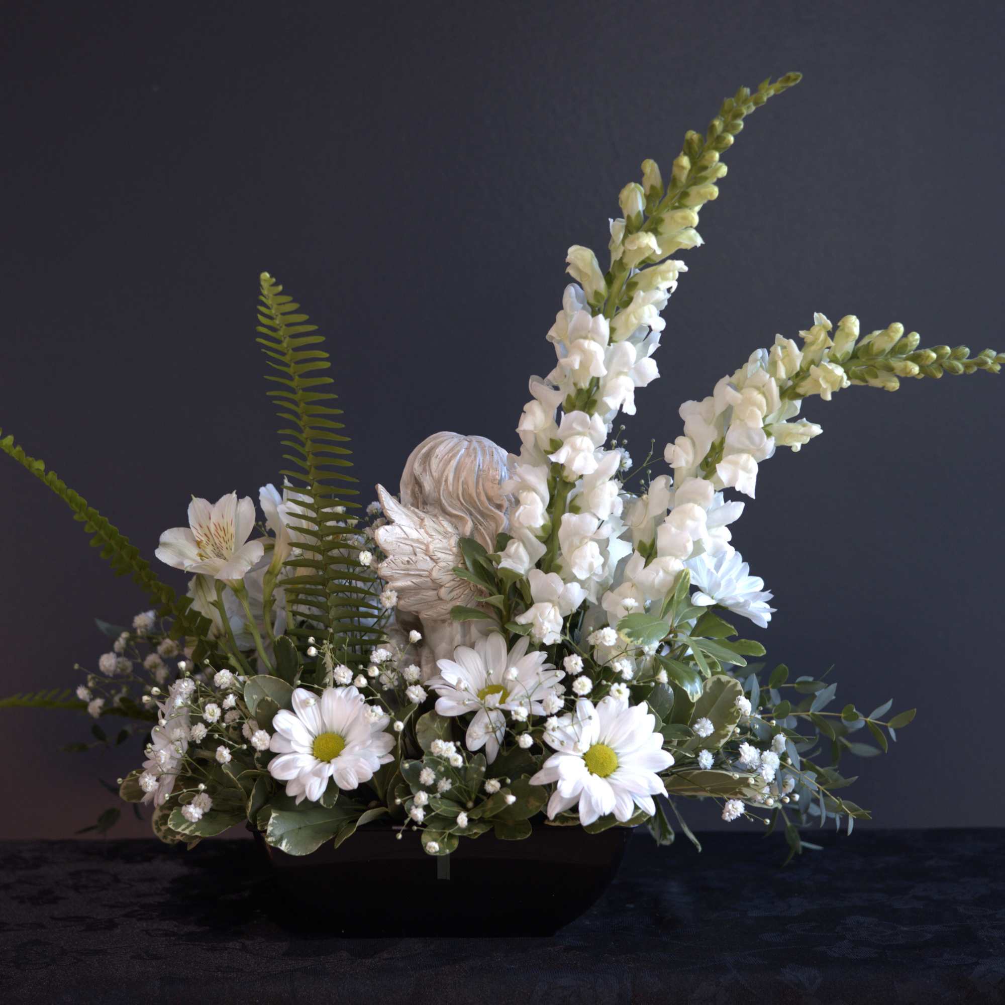 White floral arrangement with daisies and snapdragons in a black bowl