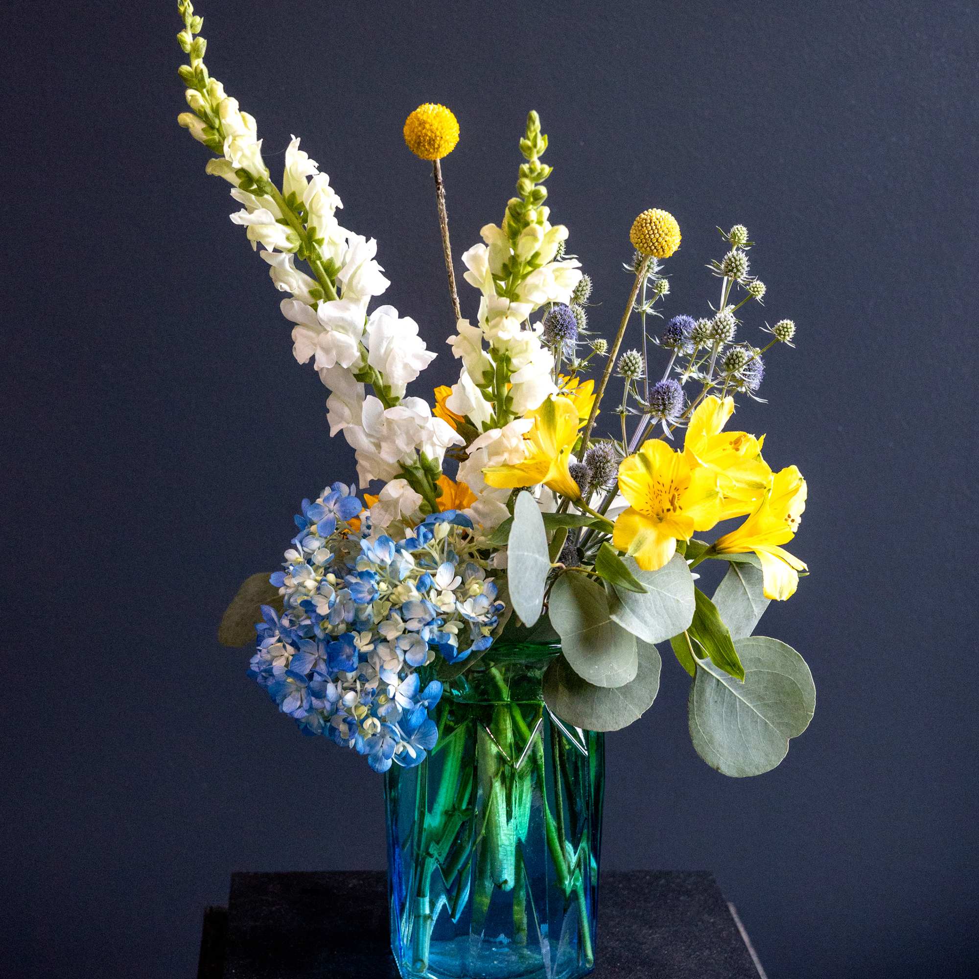 Mixed bouquet of yellow, white, and blue flowers in a blue glass vase
