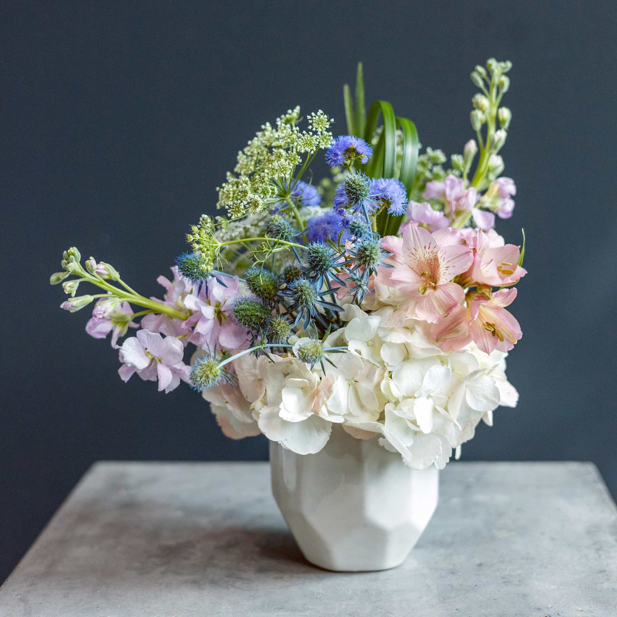 Pastel bouquet of hydrangeas, alstroemeria, and blue thistle in a white vase