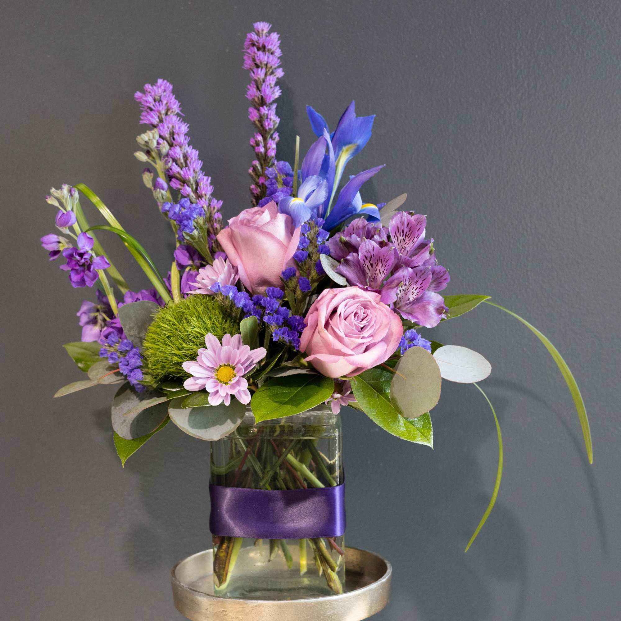 Mixture of a variety of purple florals in a glass vase decorated